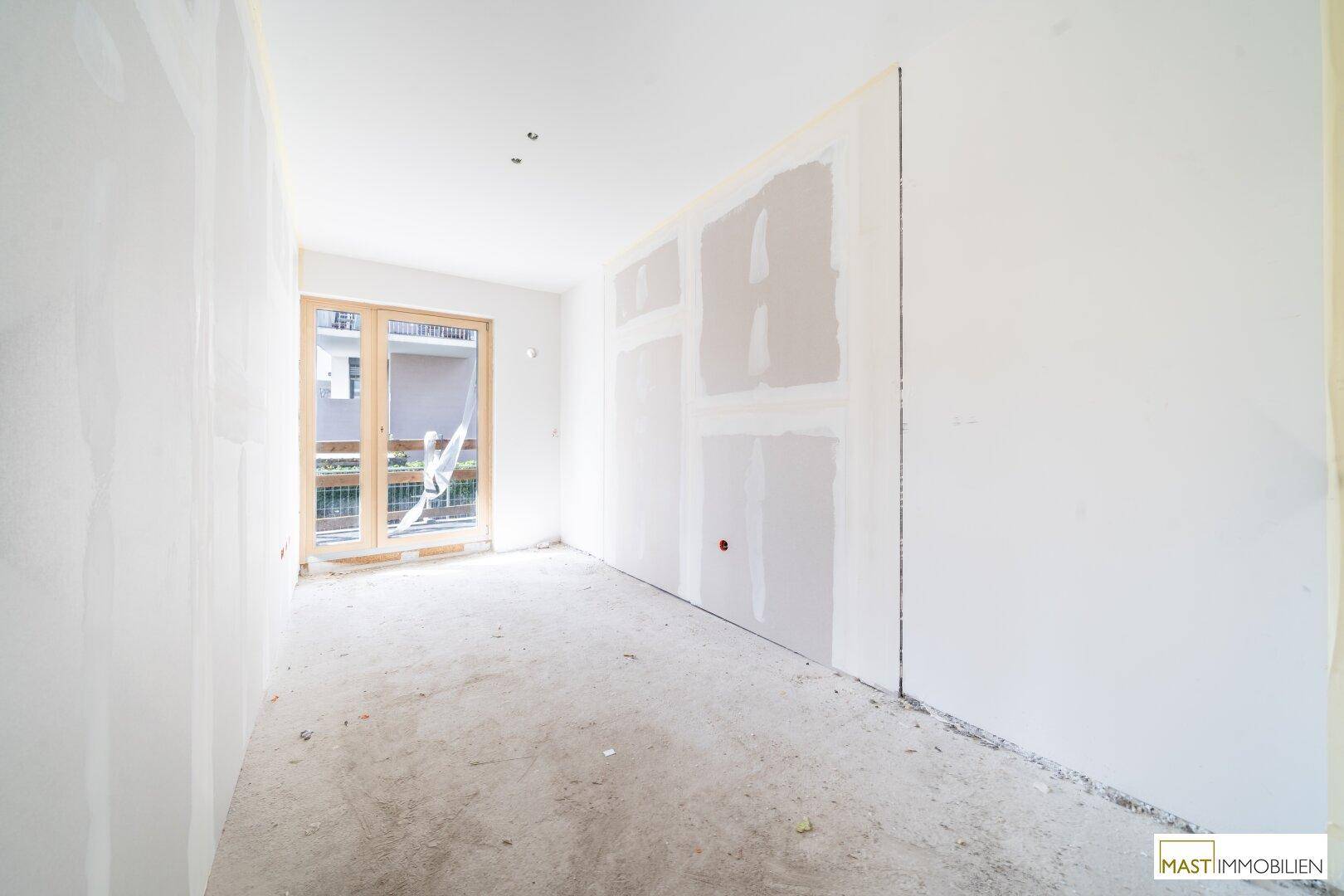 Heller, unfertiger Raum mit Betonboden und großem Fenster, bereit für die weitere Gestaltung.