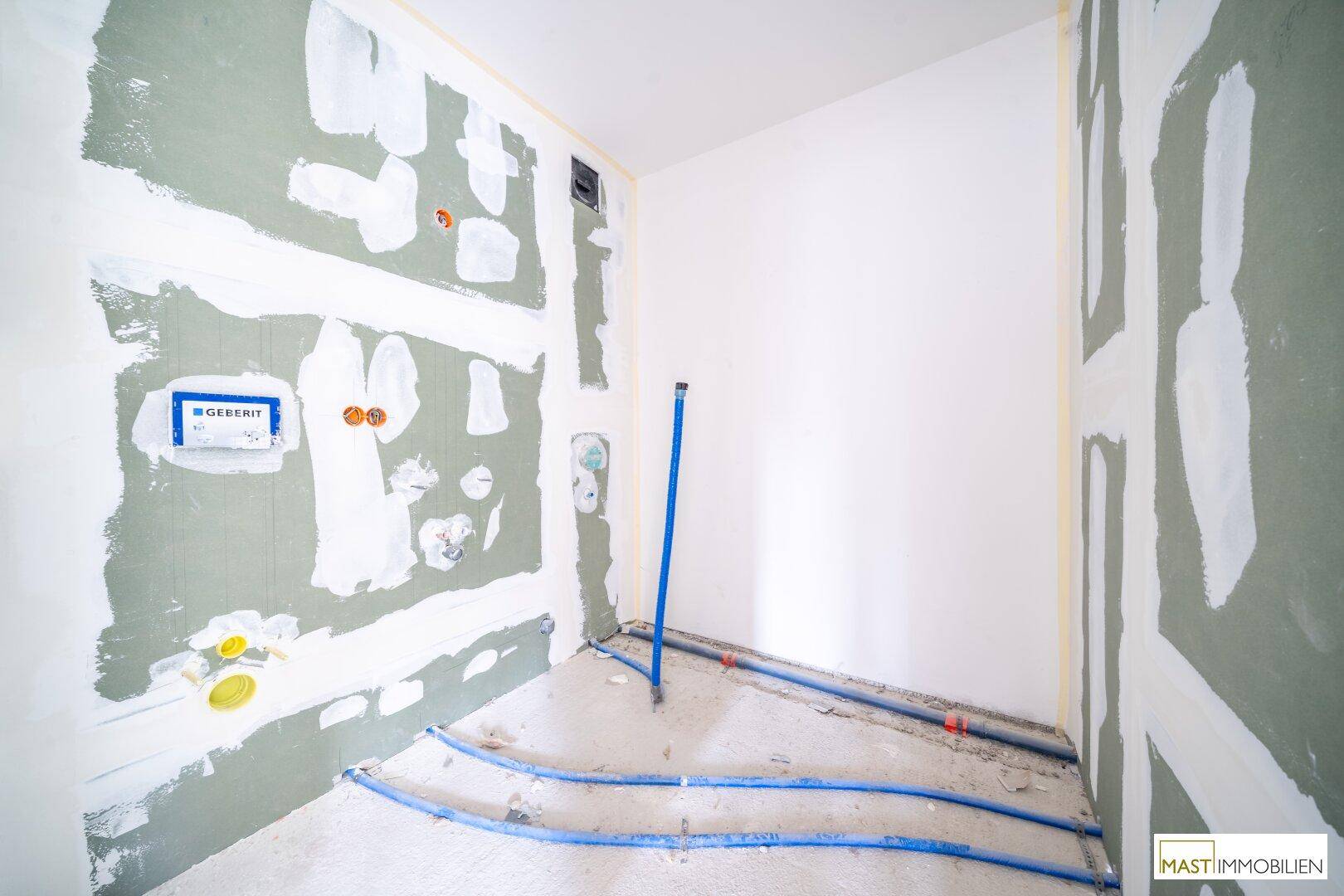 Unfertiges Badezimmer mit sichtbaren Sanitärinstallationen und Trockenbauwänden für den Ausbau.
