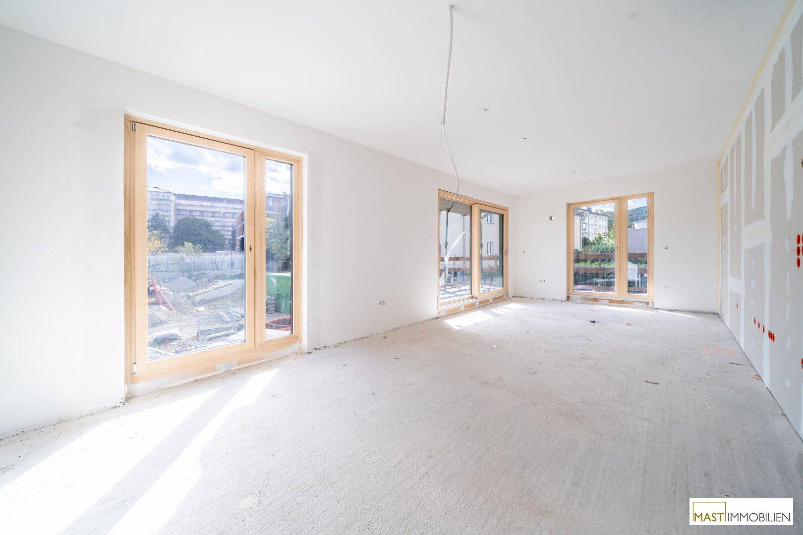 Heller, unfertiger Wohnraum mit großen Holzfenstern und Blick auf die Baustelle.