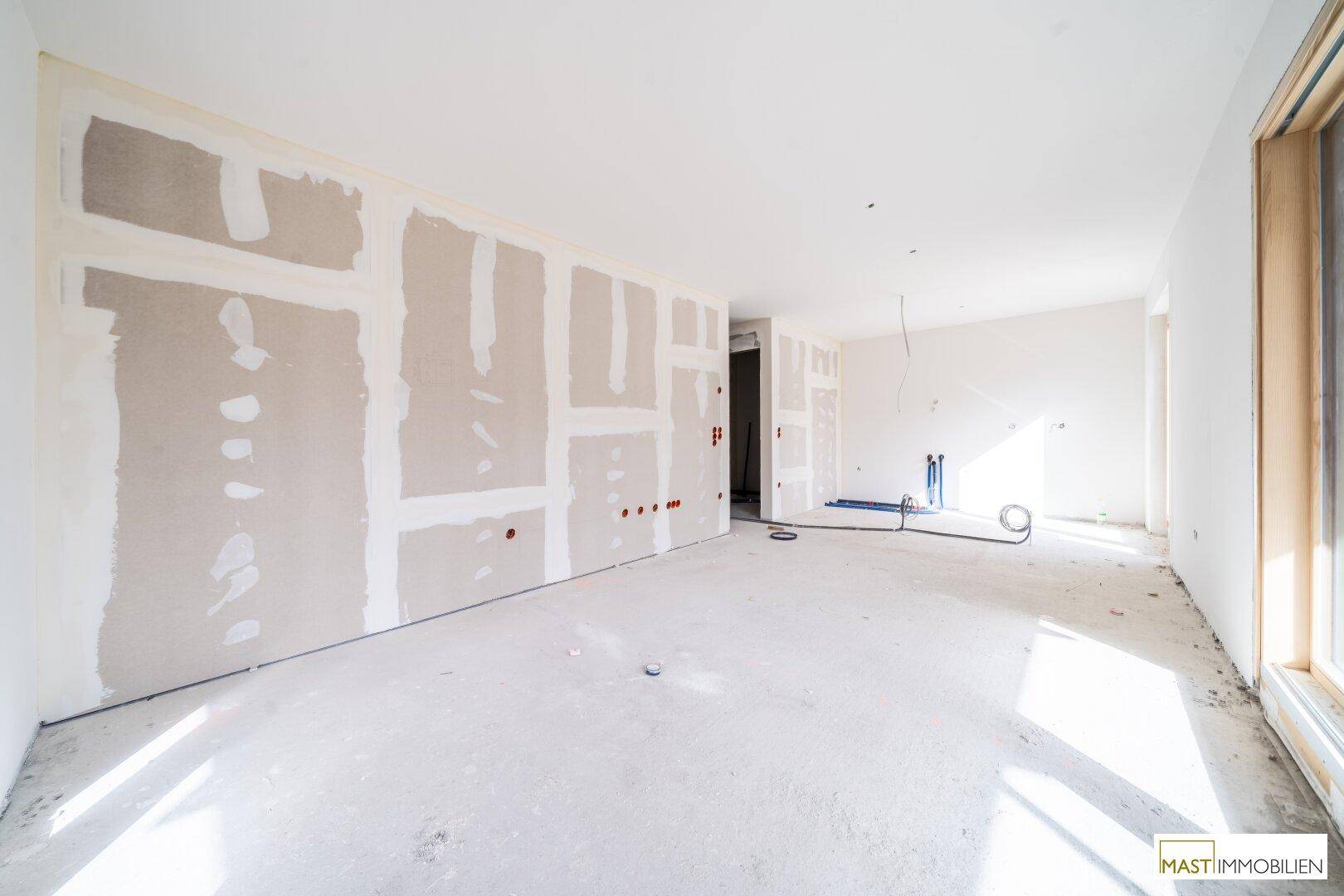 Unfertiger Innenraum mit Trockenbauwänden, Betonboden und sichtbaren Installationen im Rohbauzustand.
