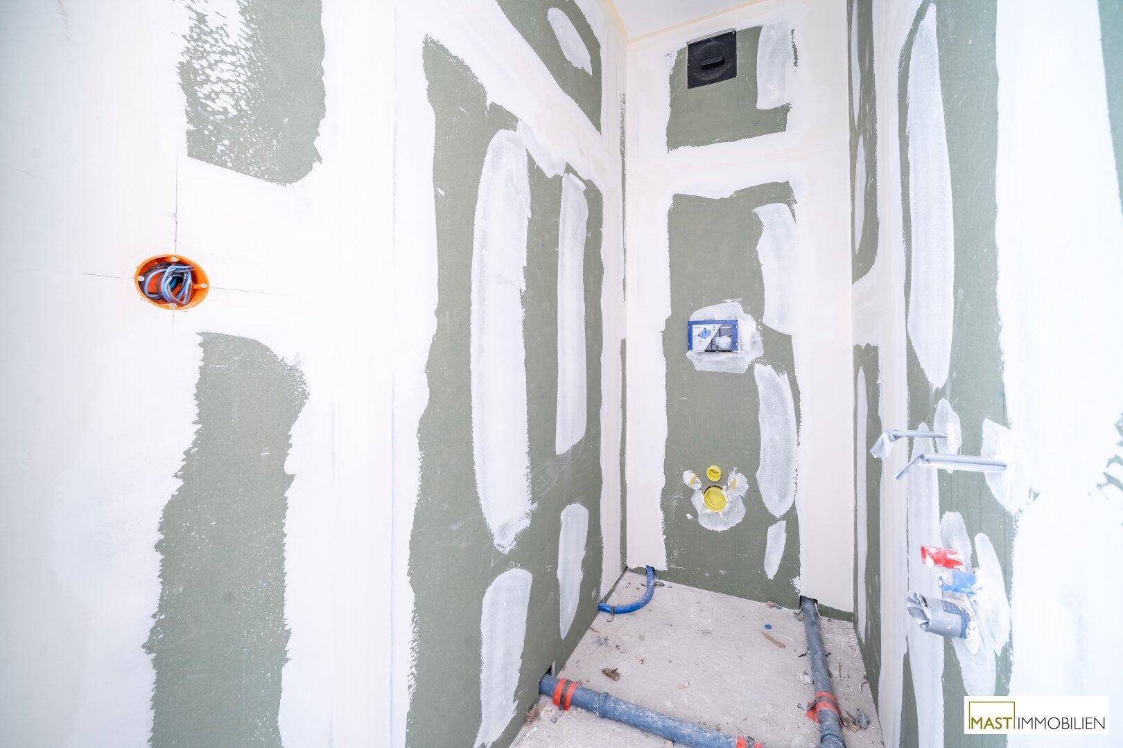 Kleiner Raum im Rohbau, vorbereitet für ein WC oder Badezimmer mit sichtbaren Wasseranschlüssen.