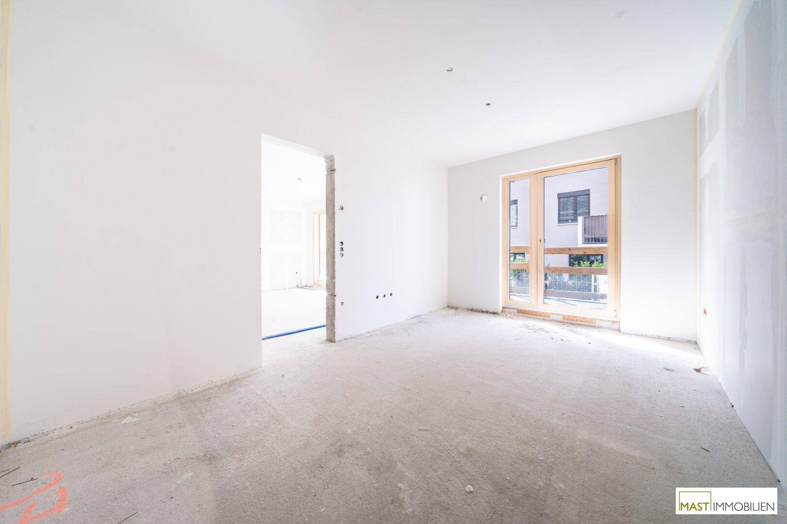 Heller Rohbau-Raum mit Betonboden und Zugang zu einem Außenbereich, bereit für den Innenausbau.