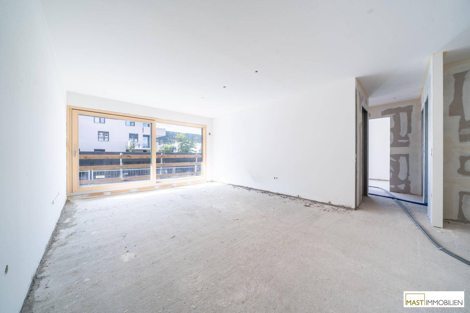 Heller Innenraum im Rohbau mit großen Fenstern und Betonboden, bereit für den Ausbau.