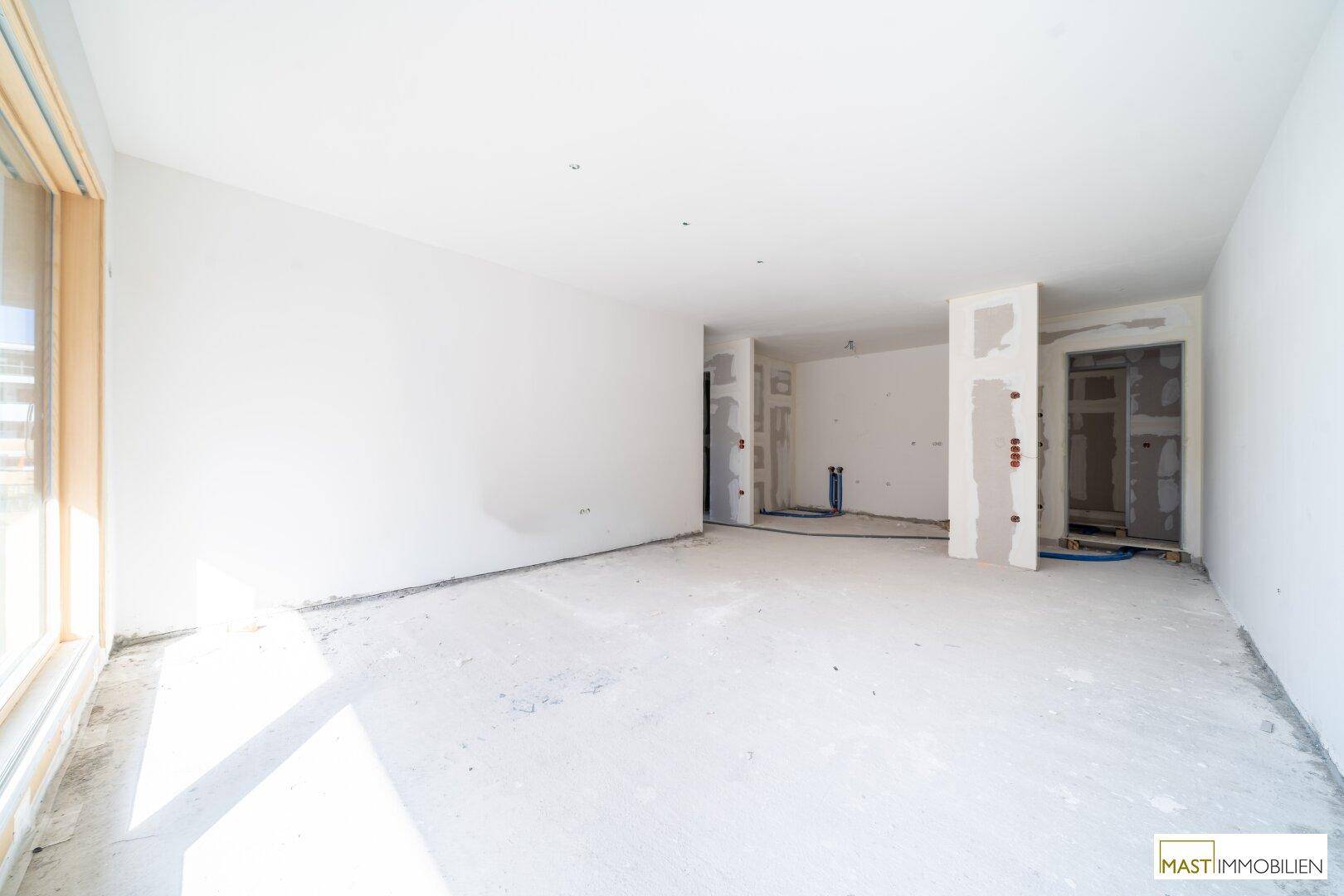 Geräumiger Innenraum im Rohbau mit viel Tageslicht und vorbereiteten Wänden für den Ausbau.