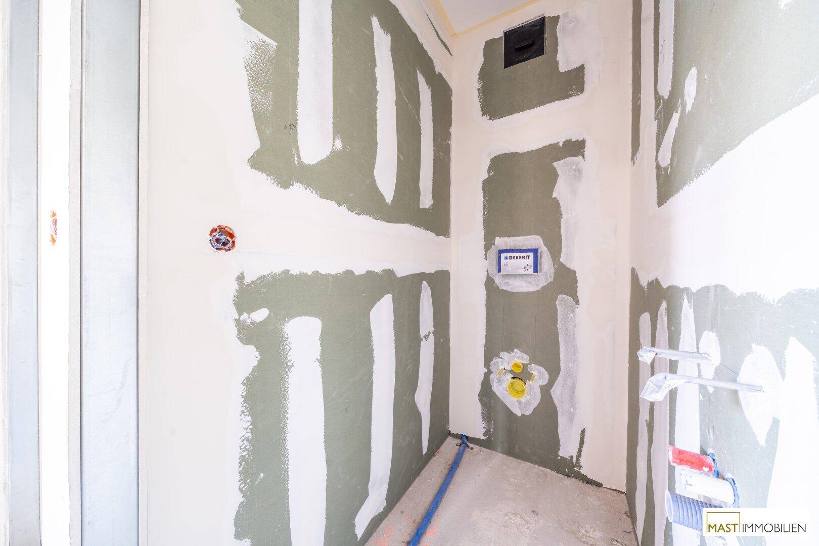 Wand im Rohbau mit Installationen für eine Wandtoilette und Waschbecken in einem Feuchtraum.