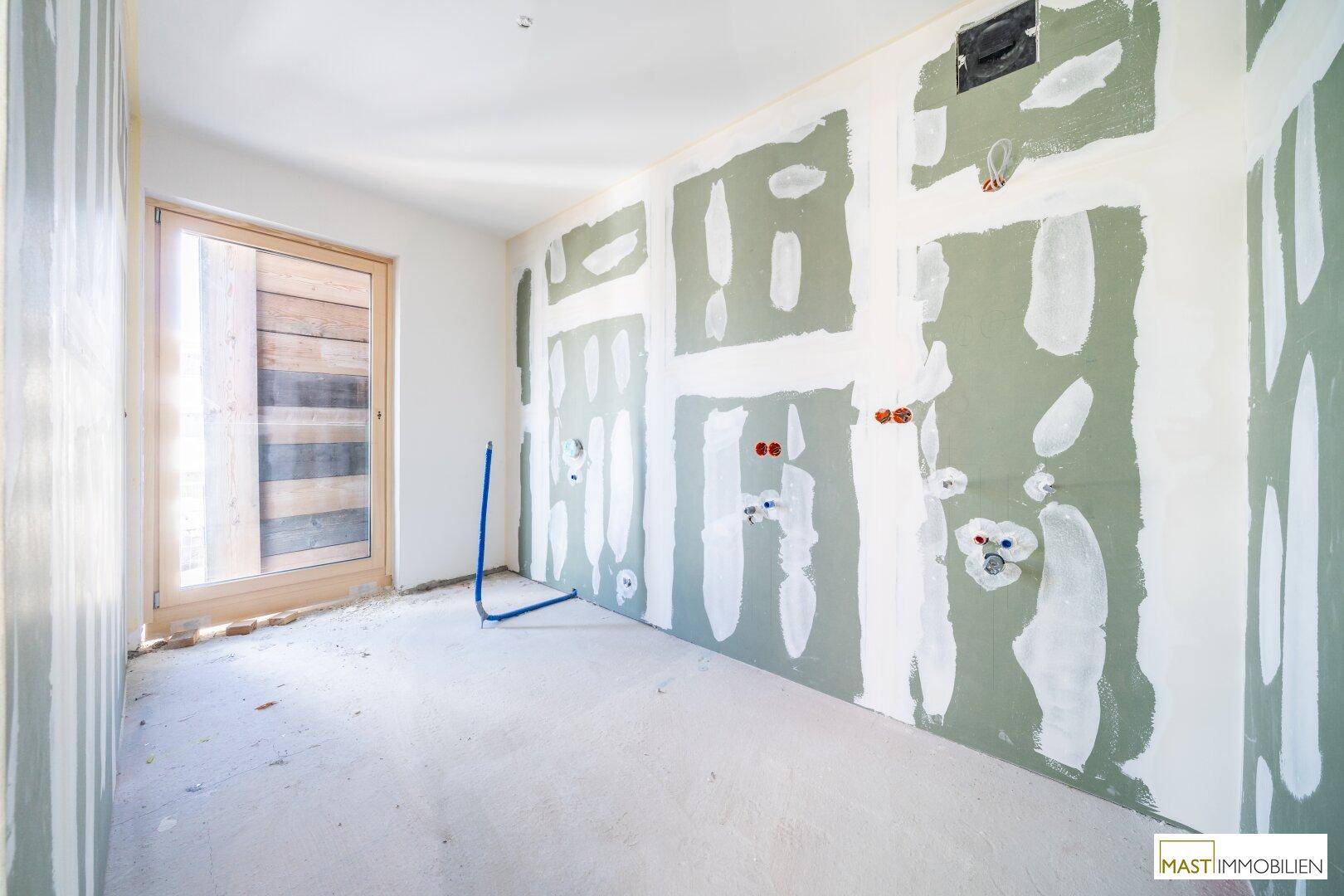 Badezimmer im Rohbau mit vorbereiteten Wänden und Fenster für natürliches Tageslicht.
