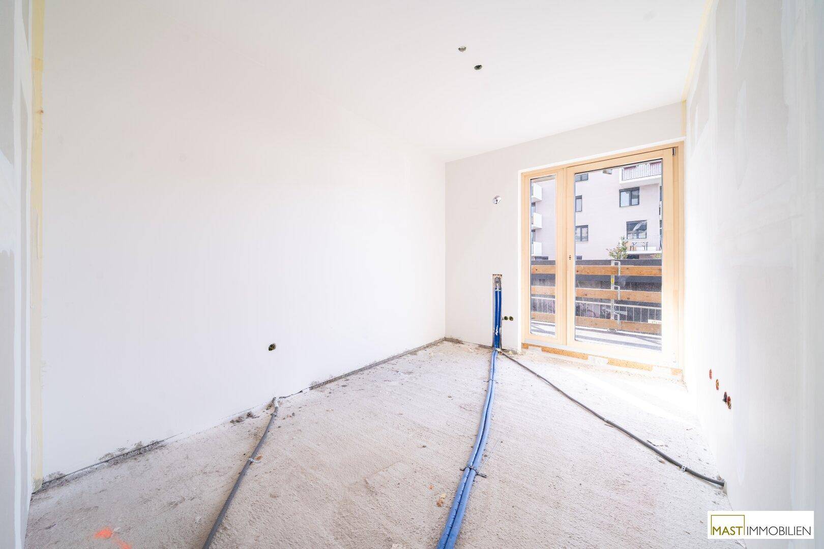 Rohbau-Innenraum mit vorbereiteten Installationen und Zugang zu einem potenziellen Außenbereich.
