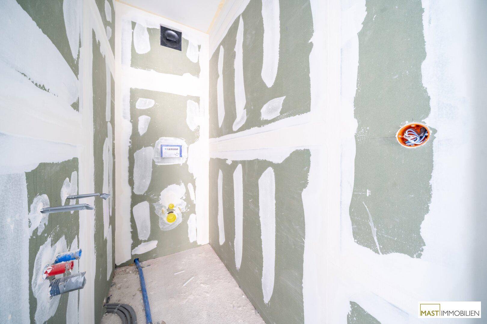 Unfertiges Badezimmer mit grünen Trockenbauwänden und Sanitärinstallationen.