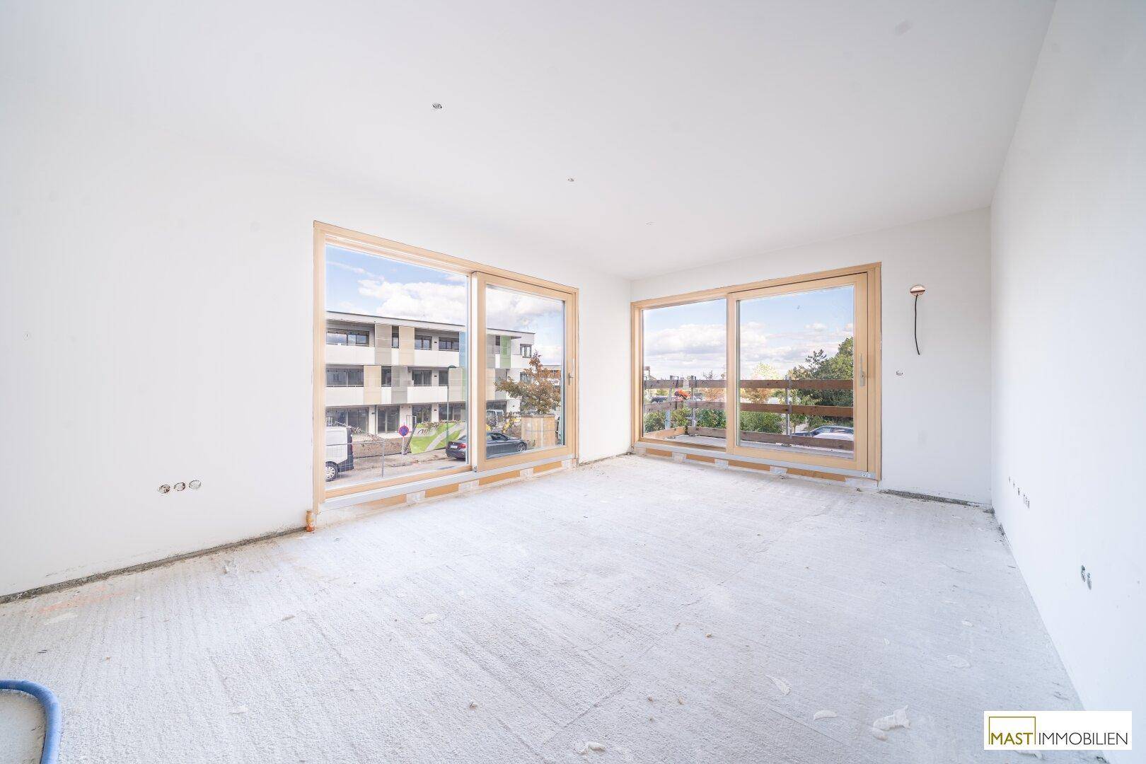 Heller, unfertiger Wohnraum mit großen Fenstern und Blick auf die Umgebung.