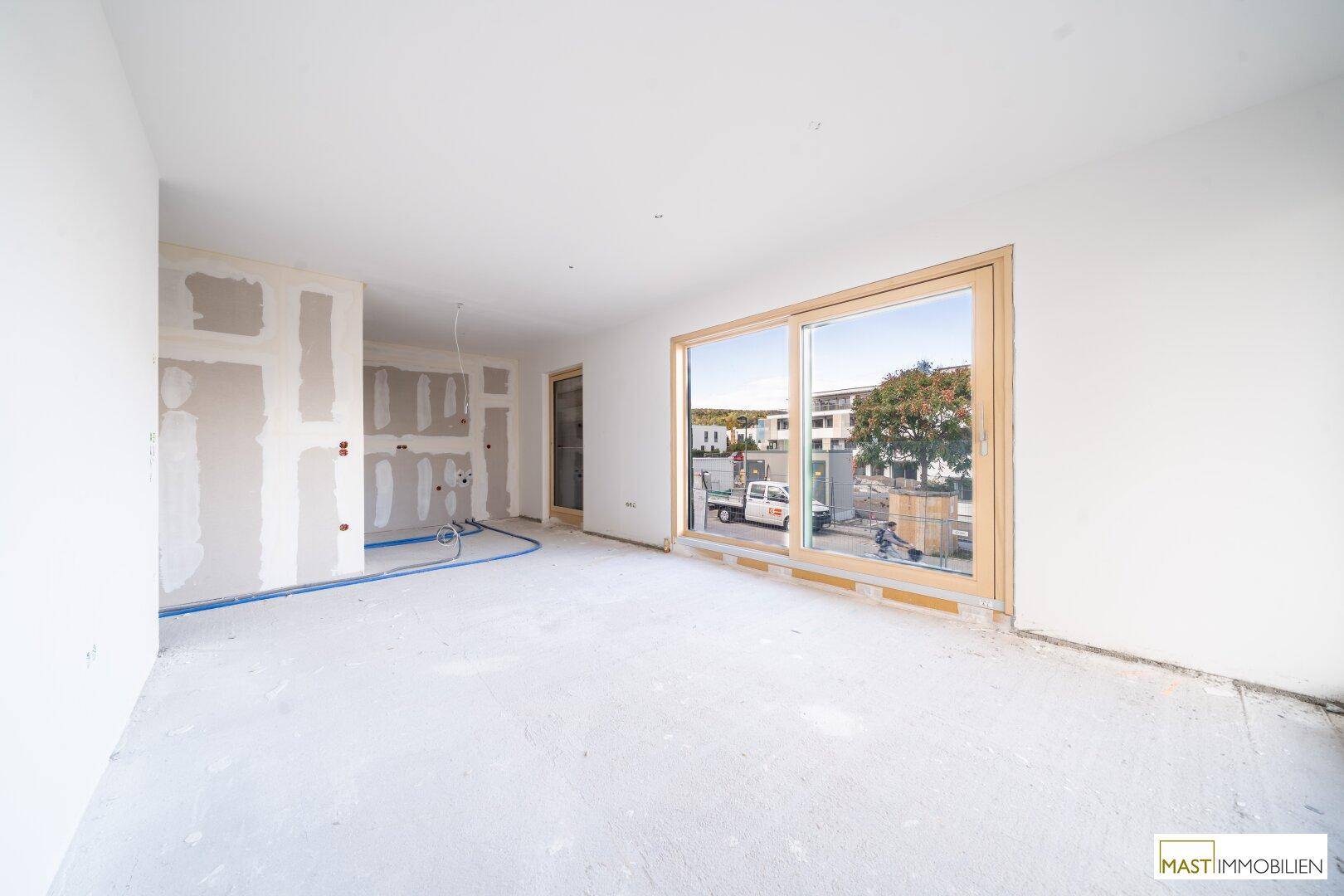 Unfertige Küche mit vorbereiteten Anschlüssen und großem Fenster zum Außenbereich.