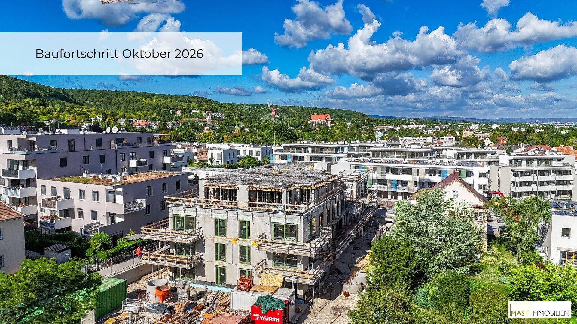 Panoramablick auf ein Neubauprojekt mit umliegenden Häusern und bewaldeten Hügeln.