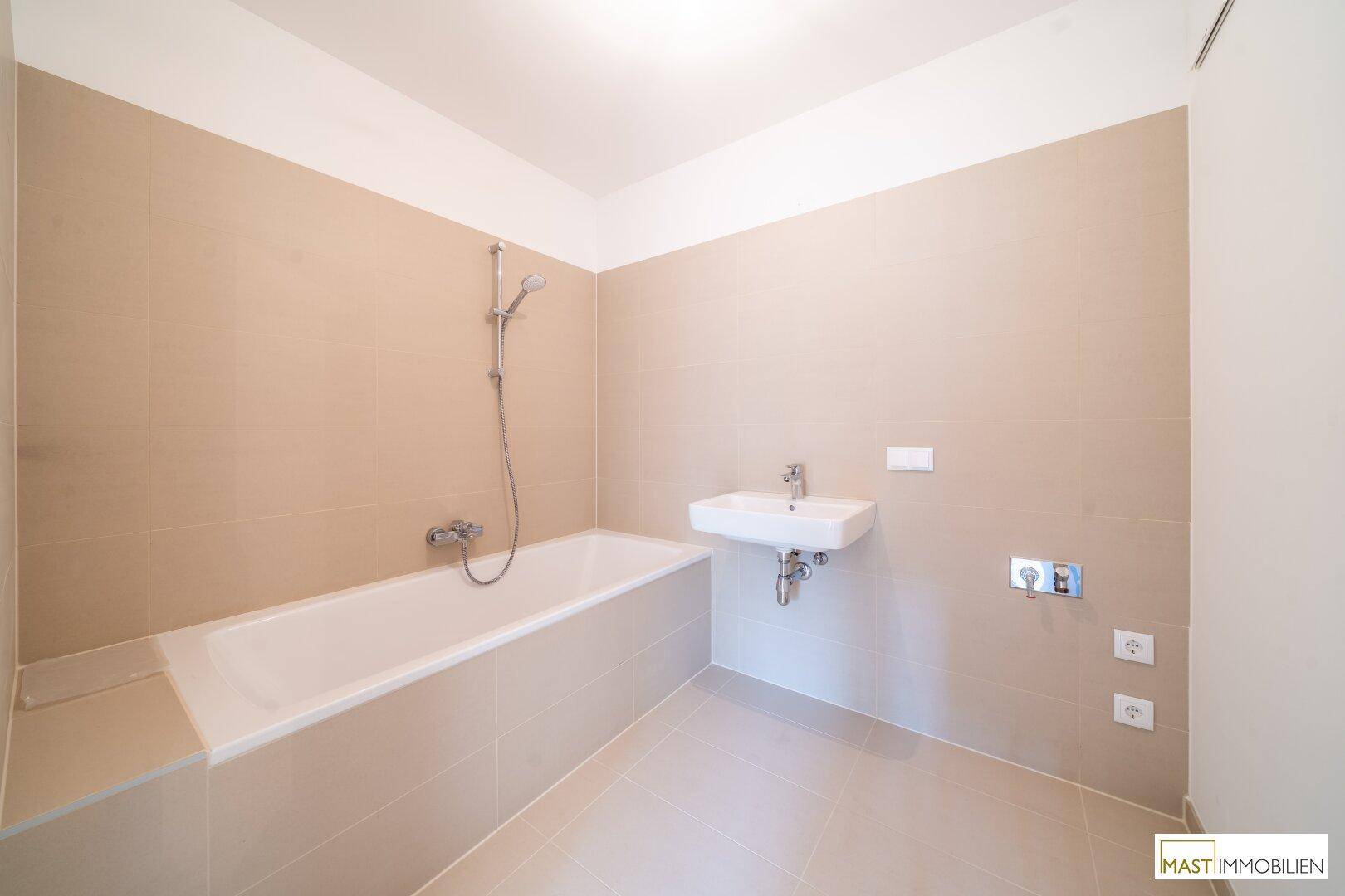 Modernes Badezimmer mit Badewanne, Waschbecken und beigefarbenen Fliesen, bereit zur Nutzung.