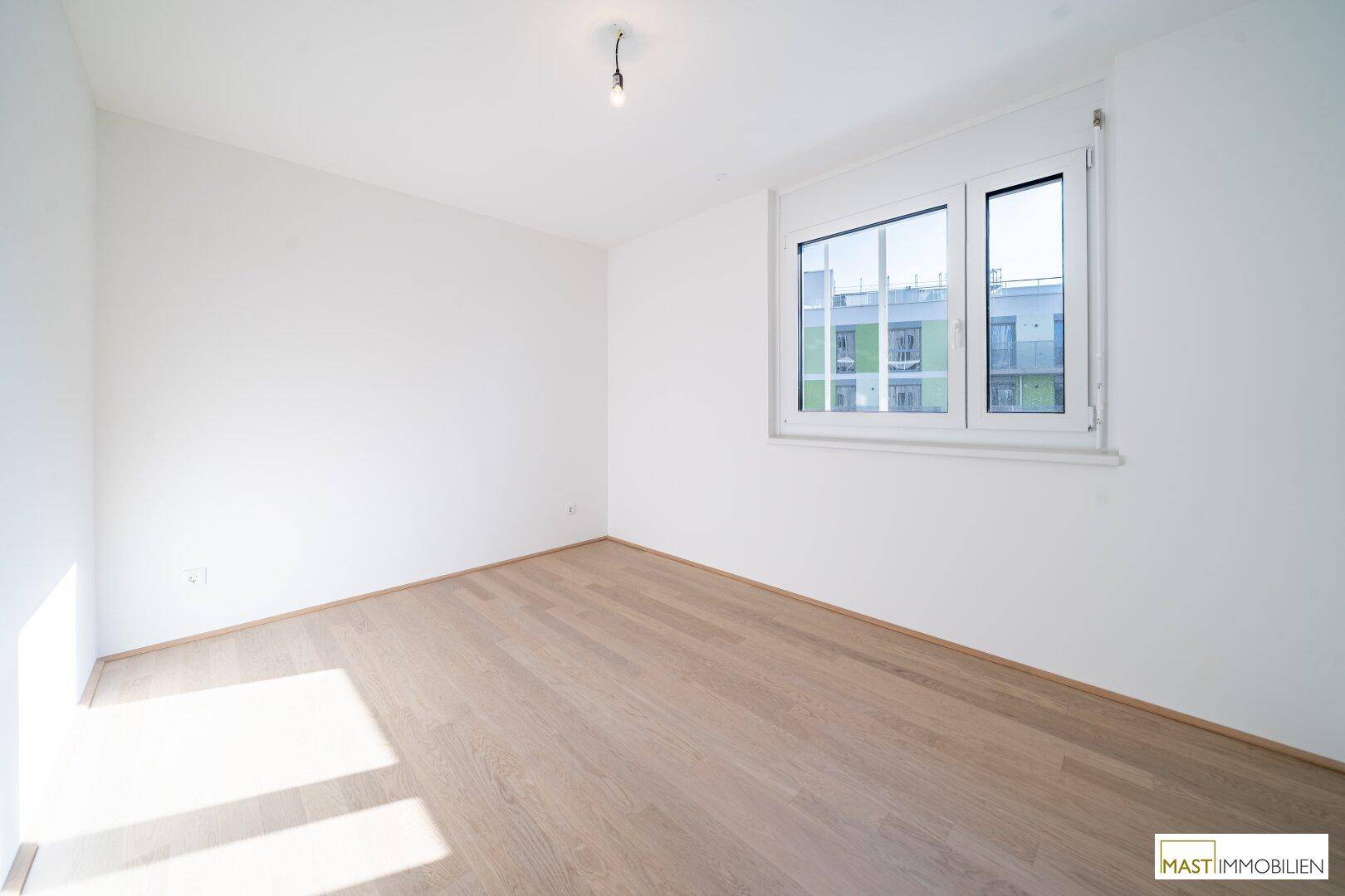 Helles Schlafzimmer mit Parkettboden und Fenster, das einen Blick auf die Umgebung bietet.