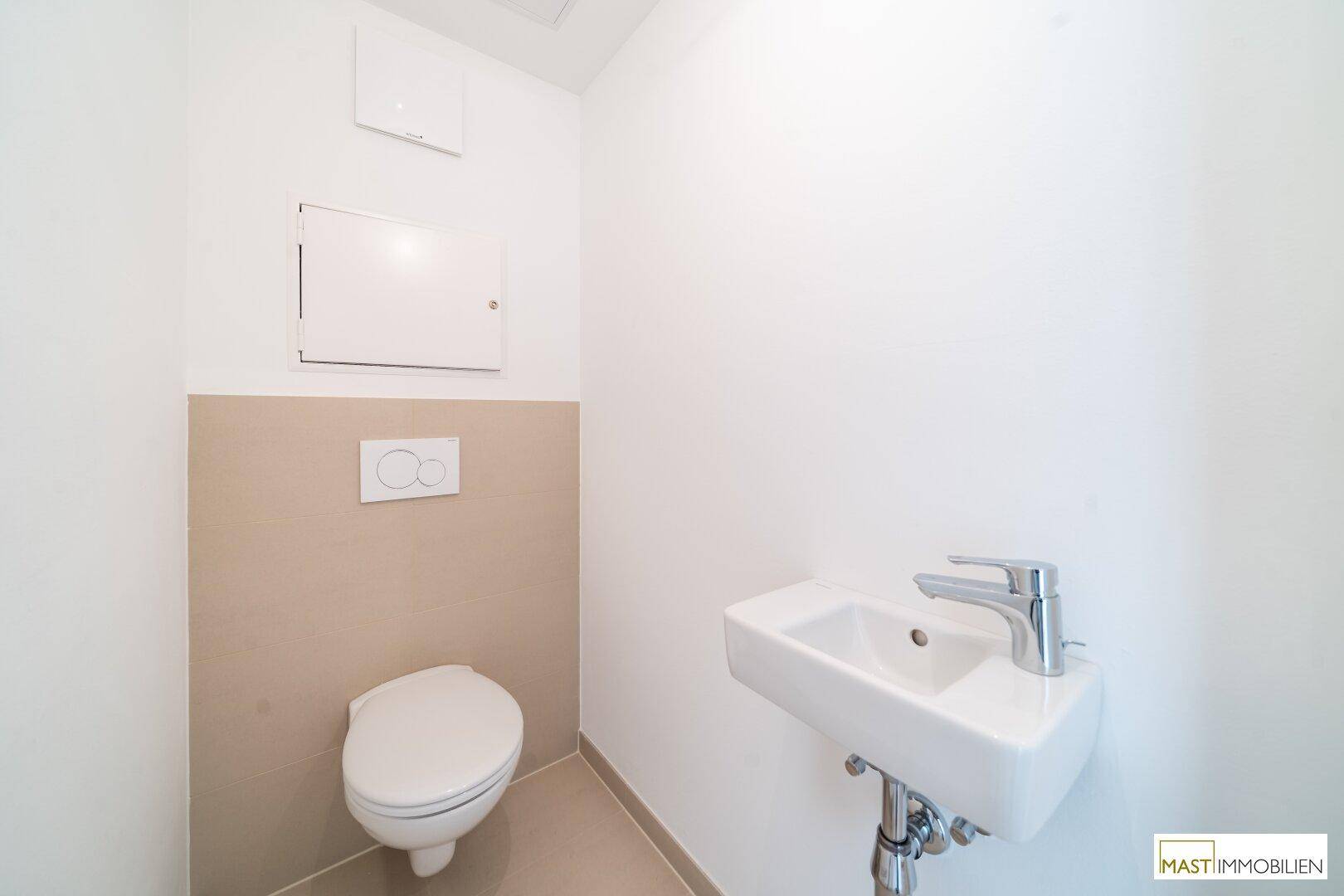 Separates WC mit wandhängender Toilette und kleinem Waschbecken, sauber und funktional.