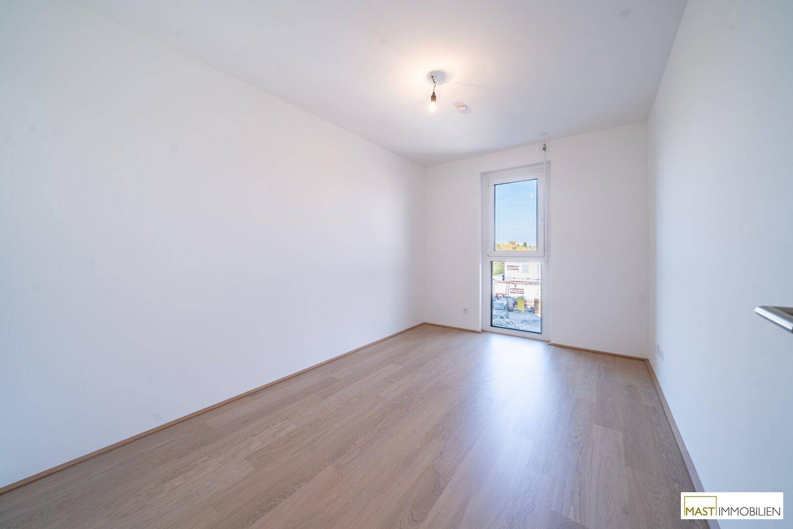 Helles Schlafzimmer mit Parkettboden und großem Fenster, bietet viel Tageslicht und eine angenehme Atmosphäre.