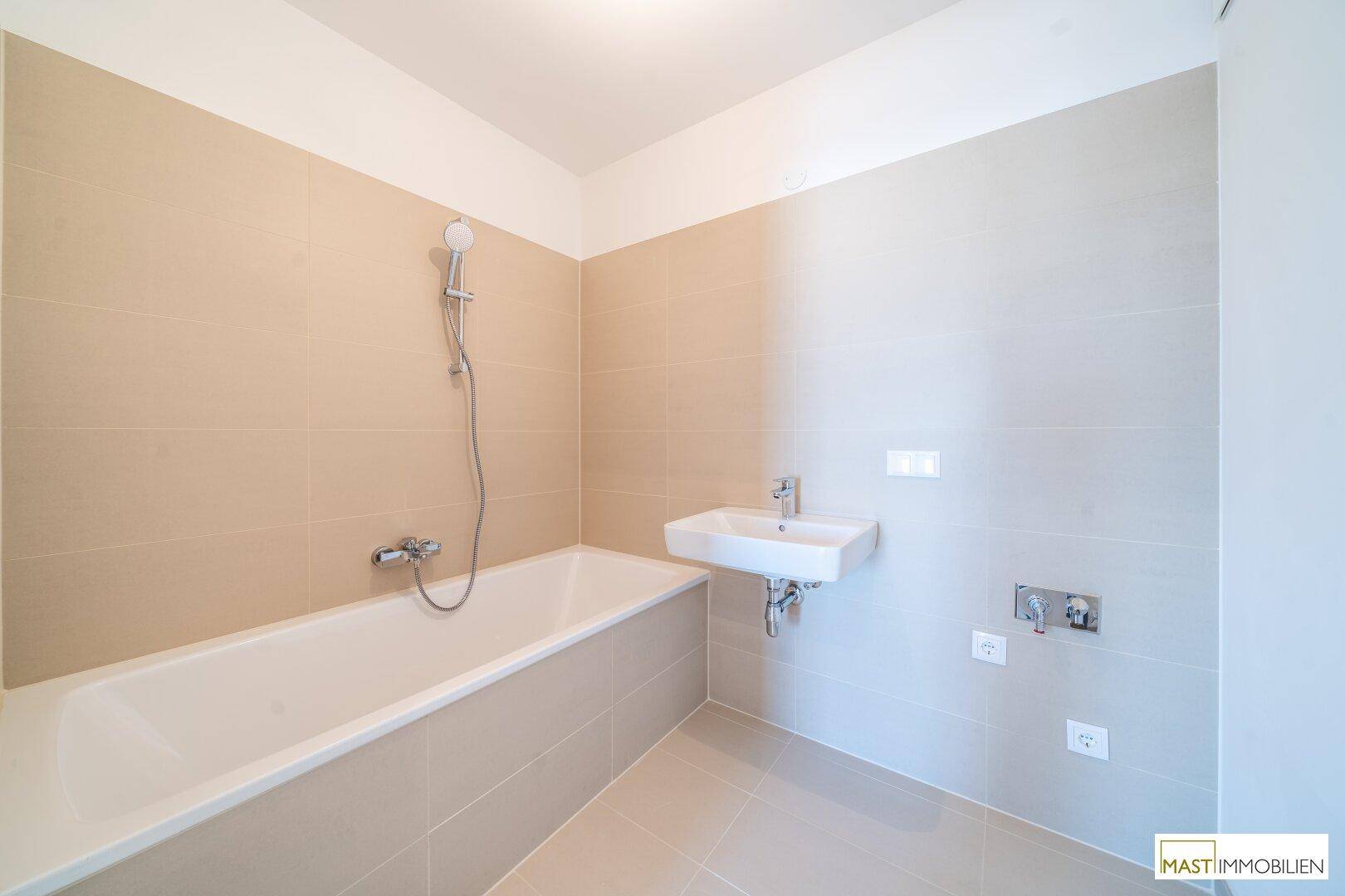 Modernes Badezimmer mit Badewanne, Waschbecken und beigefarbenen Fliesen, in neuwertigem Zustand.