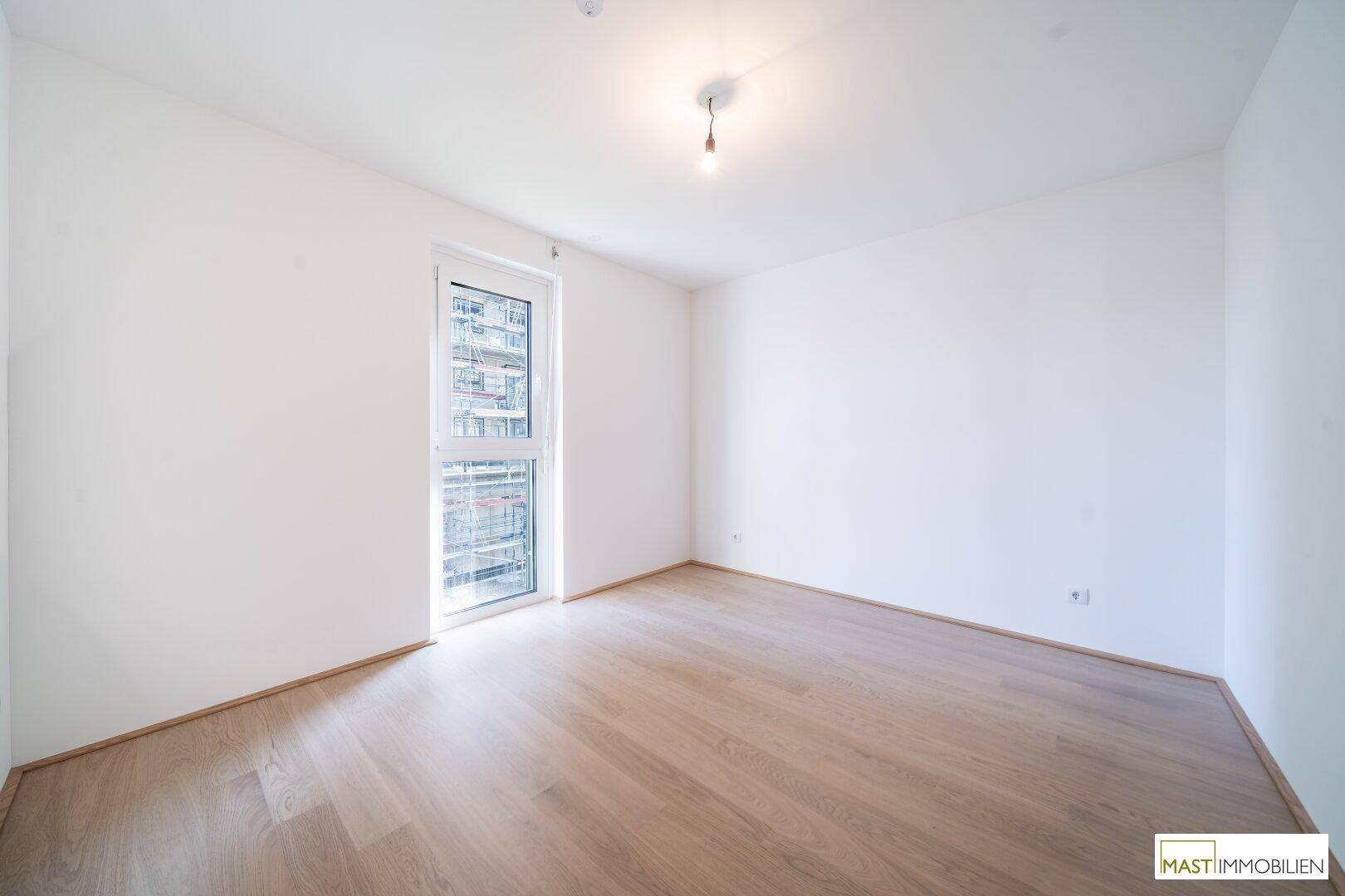 Leeres Schlafzimmer mit Parkettboden und Fenster, ideal für ein Kinder- oder Gästezimmer in neuwertigem Zustand.