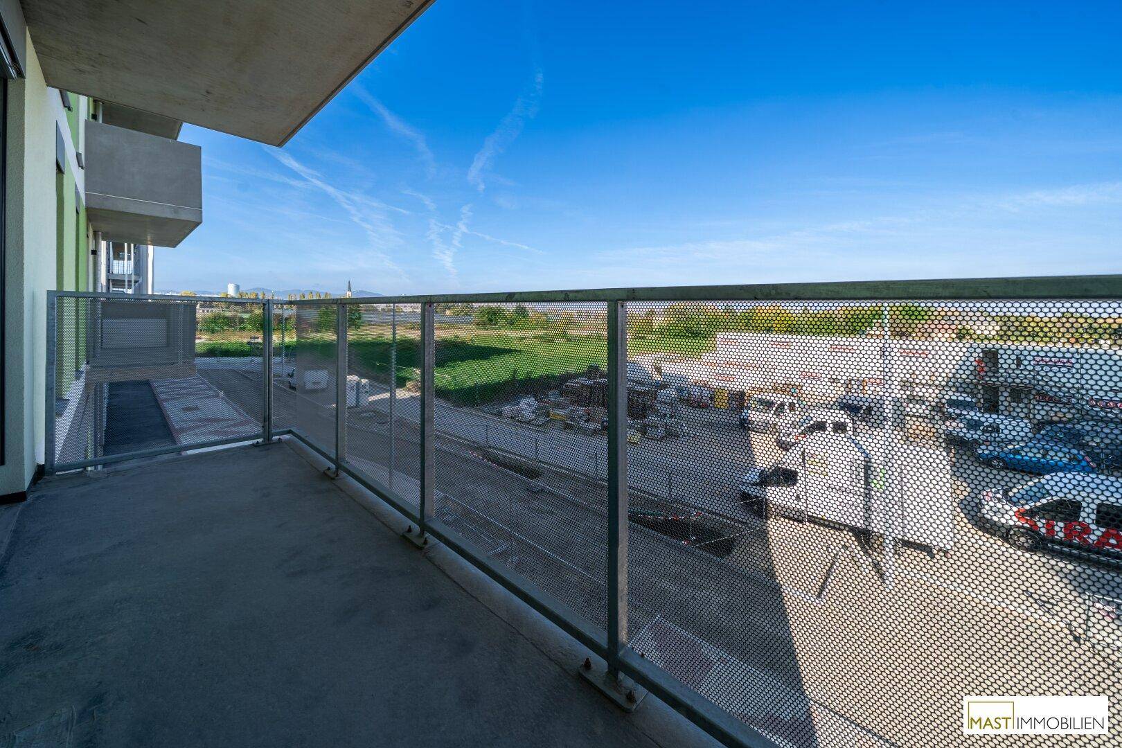 Geräumiger Balkon mit Metallgeländer und weitem Blick auf die Umgebung und grüne Flächen.