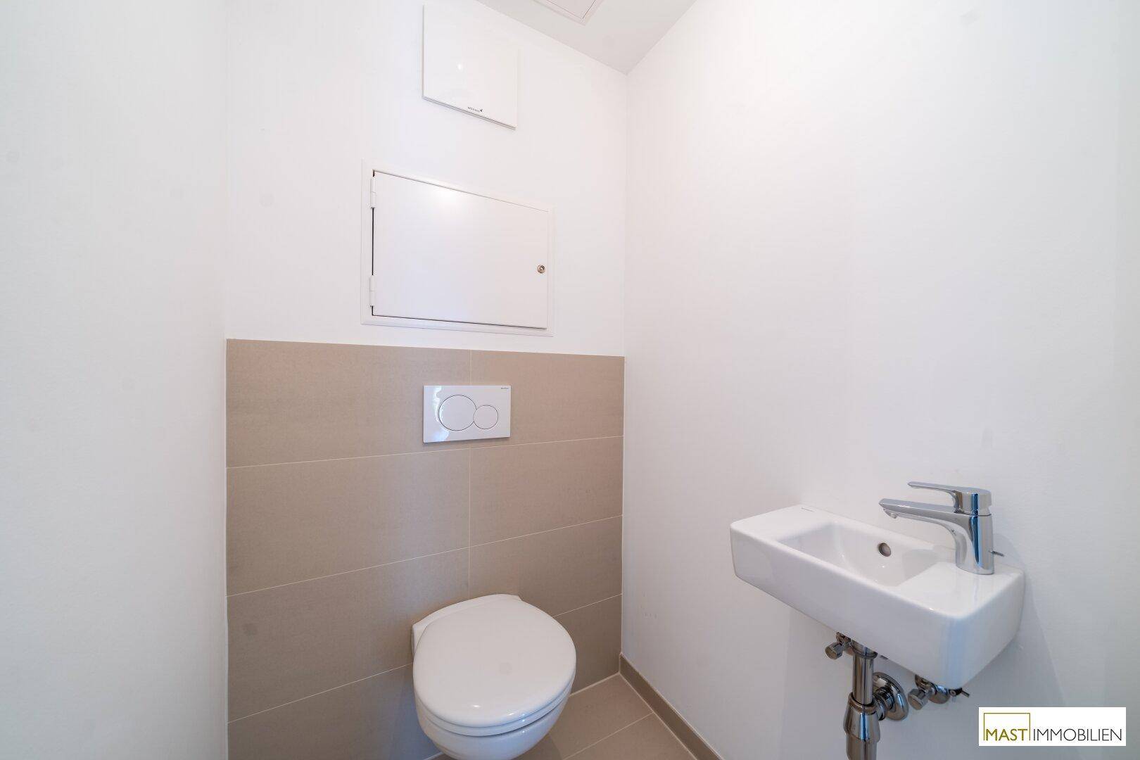 Separates Gäste-WC mit wandhängender Toilette und kleinem Waschbecken, in modernem Design.