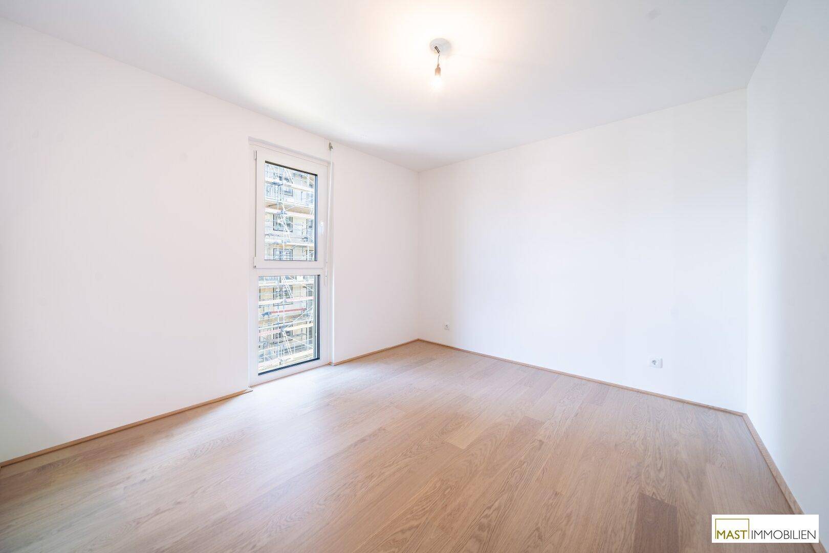 Leeres Schlafzimmer mit Parkettboden und großem Fenster, ideal für ein Kinder- oder Gästezimmer.