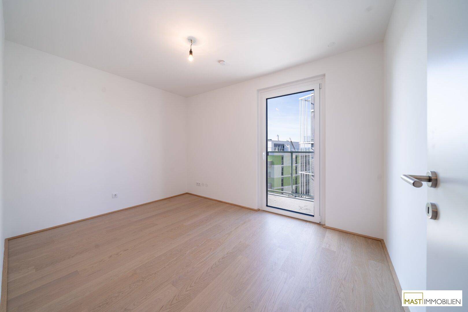 Unmöbliertes Schlafzimmer mit Parkettboden und Zugang zu einem französischen Balkon.