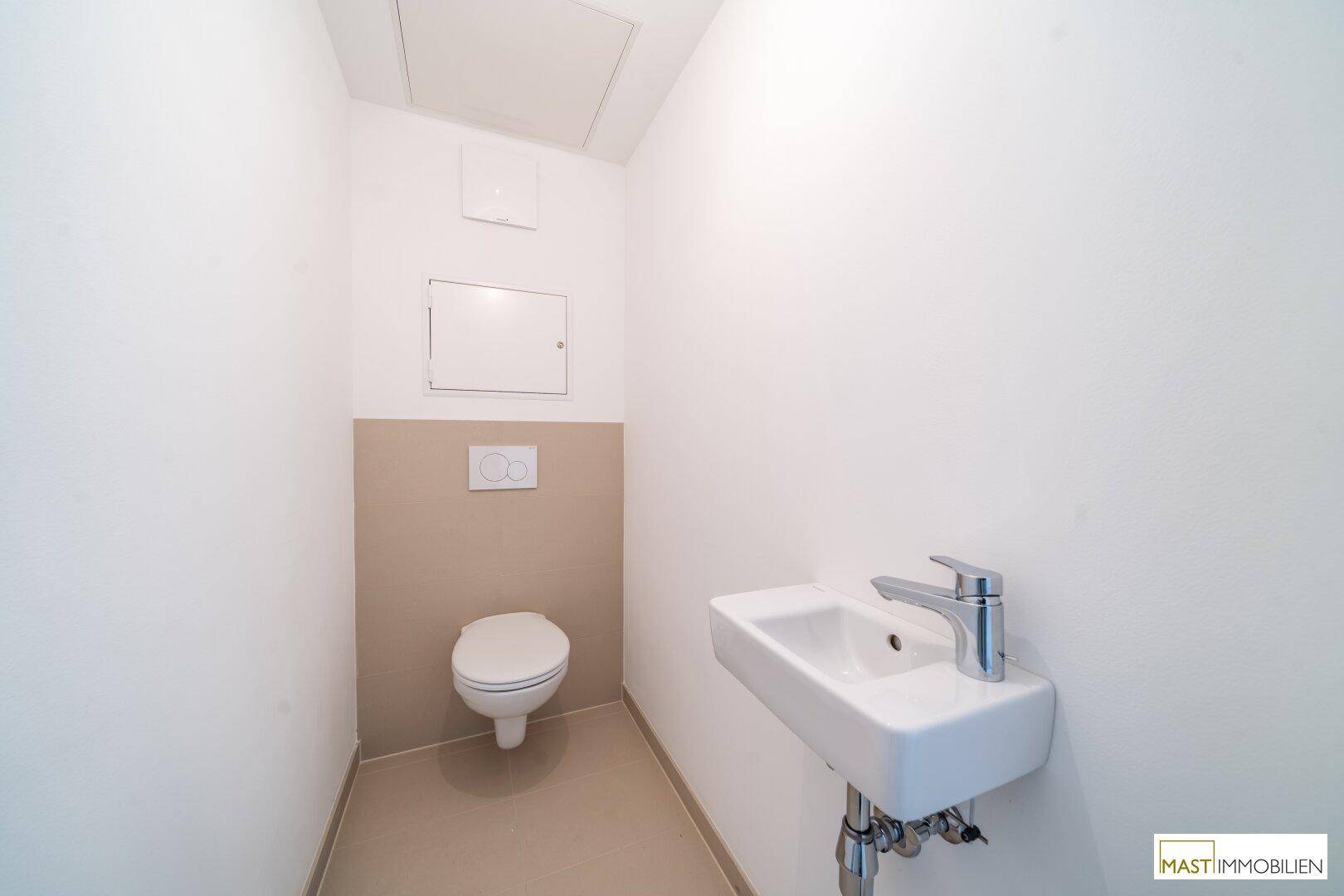 Separates Gäste-WC mit wandhängender Toilette und kleinem Handwaschbecken.
