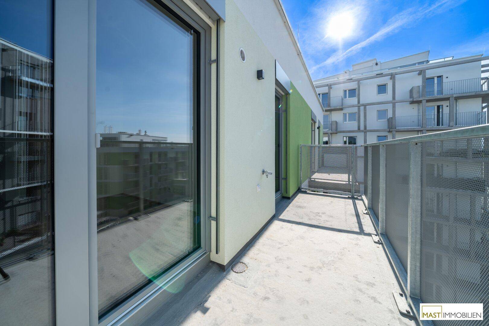 Sonniger Balkon mit Metallgeländer und Blick auf die moderne Wohnbebauung.