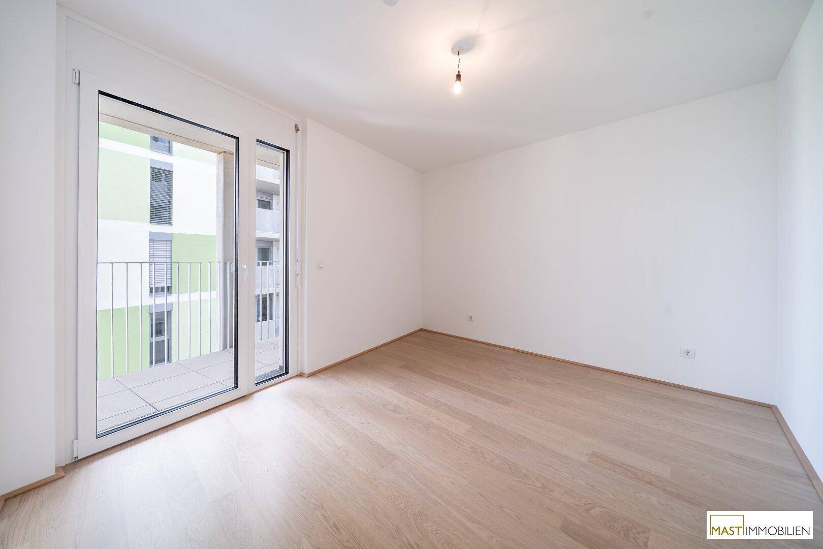 Leeres Zimmer mit hellem Holzboden und direktem Zugang zu einem Außenbereich, ideal als Schlafzimmer.