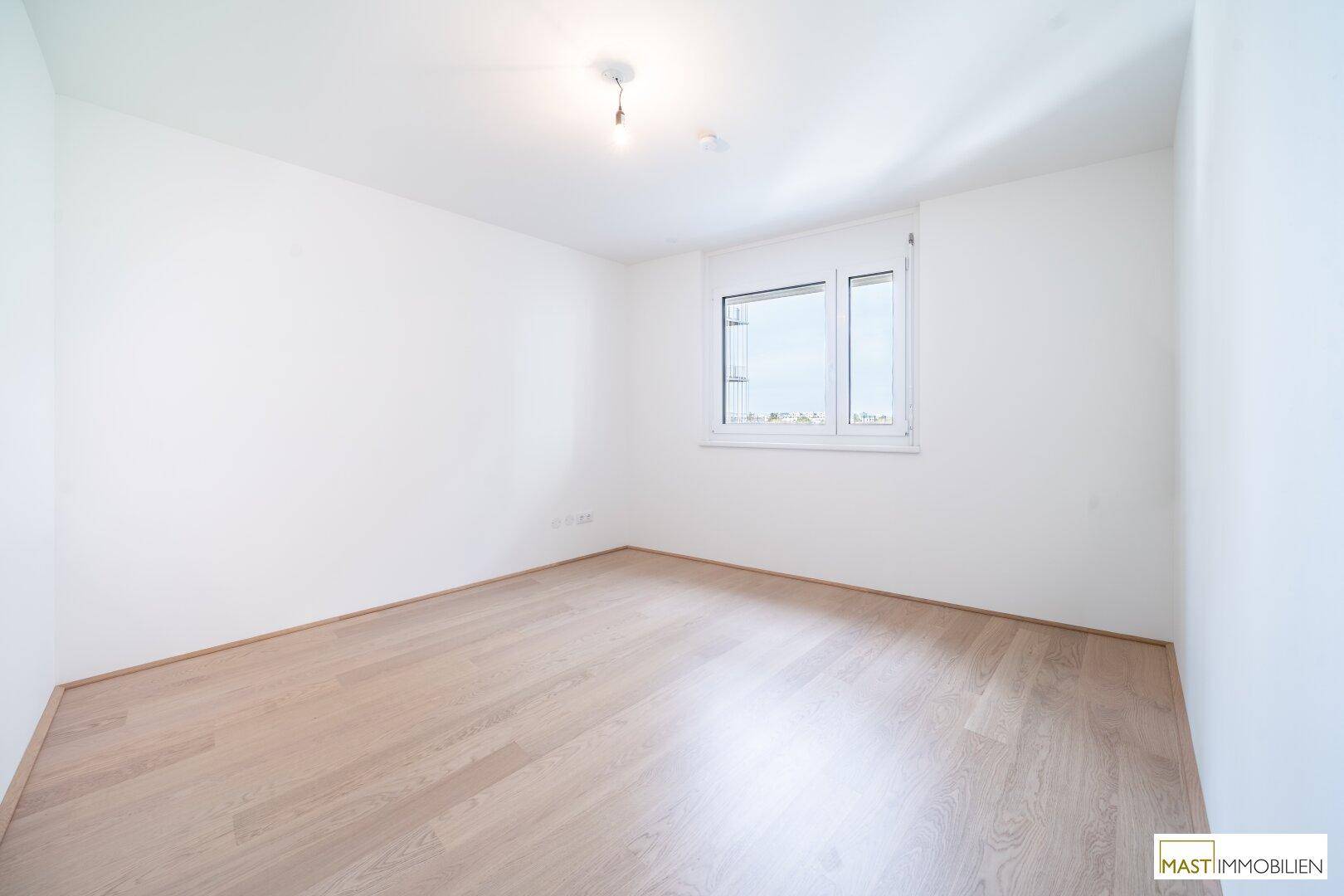 Unmöbliertes Zimmer mit großen Fenstern und hellem Parkettboden, bietet viel Tageslicht.