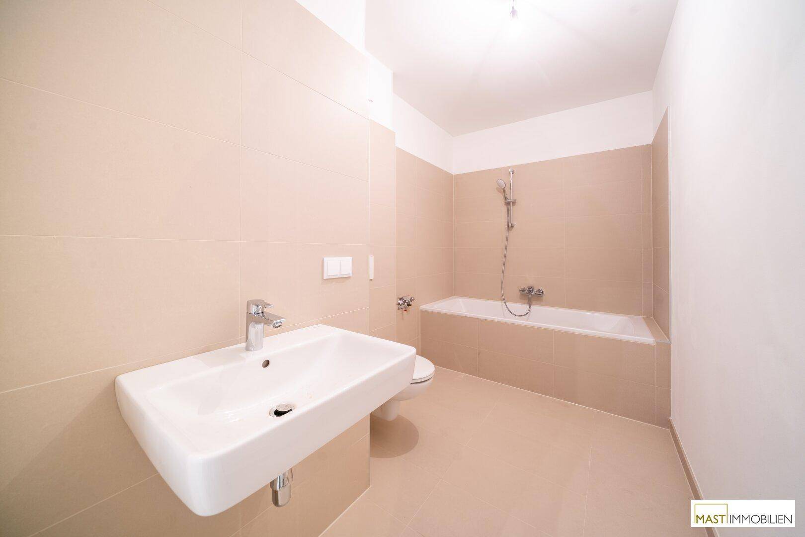 Modernes Badezimmer mit Badewanne, Waschbecken und beigefarbenen Fliesen an den Wänden.