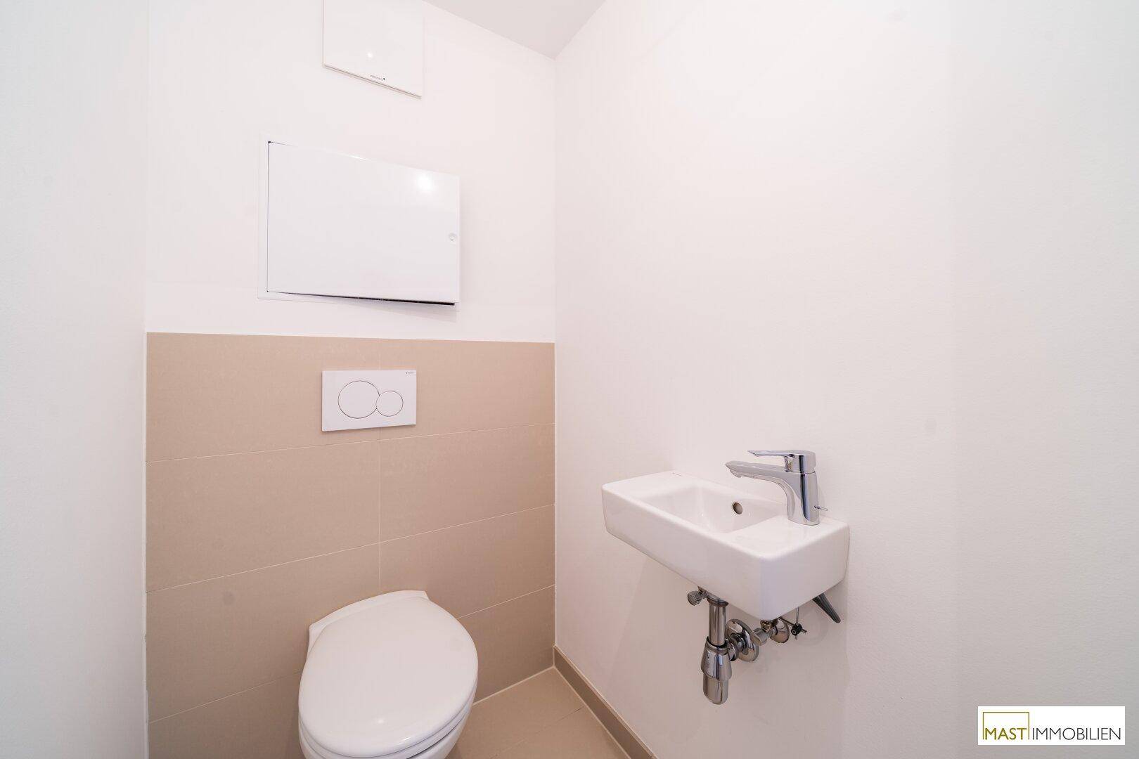 Separate Gästetoilette mit Wand-WC und kleinem Waschbecken, halbhoch gefliest in Beige.