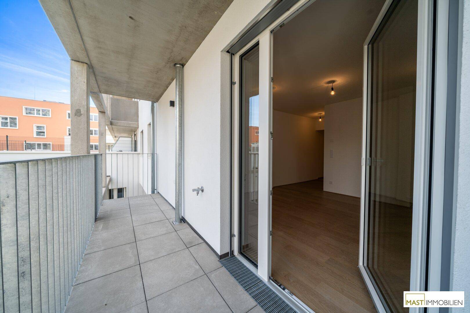Geräumiger Balkon mit Zugang zum Innenraum und Blick auf die umliegenden modernen Gebäude.