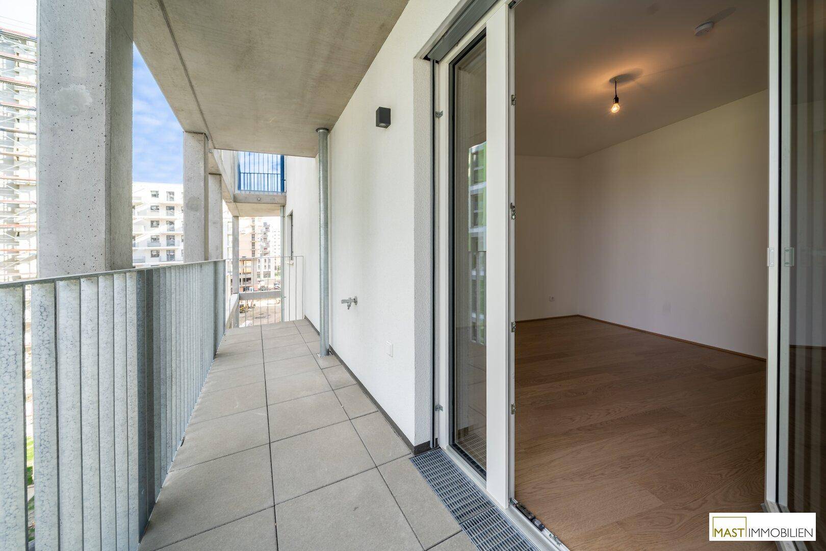 Heller Balkon mit Fliesenboden und Blick auf die moderne Wohnanlage und den Himmel.