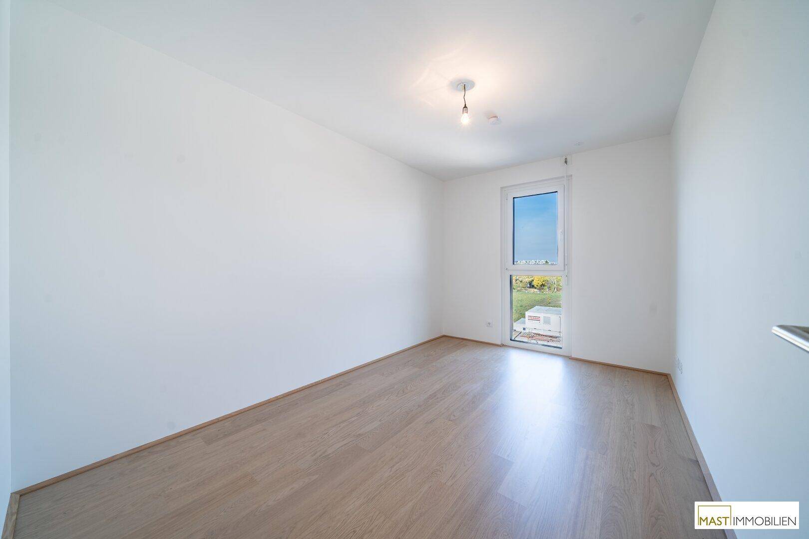 Helles Zimmer mit Parkettboden und einem Fenster mit Blick ins Grüne, ideal als Schlaf- oder Arbeitszimmer.