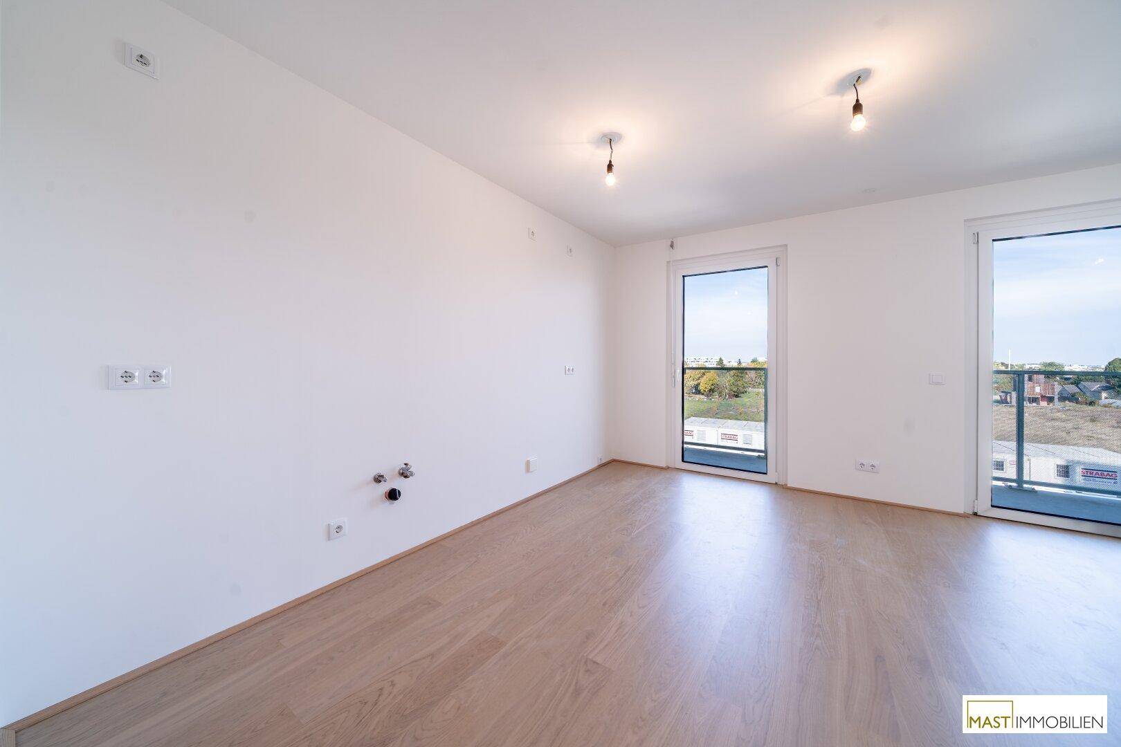 Heller Raum mit Anschlüssen für eine Küche und hellem Parkettboden, bereit für die Installation.
