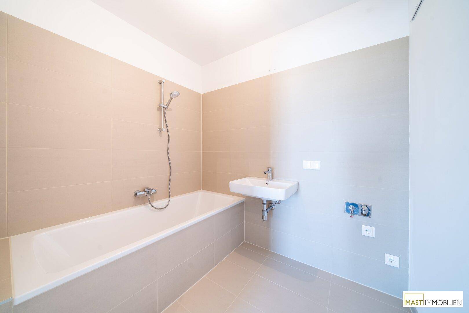 Modernes Badezimmer mit beigefarbenen Fliesen, Badewanne und Waschbecken.