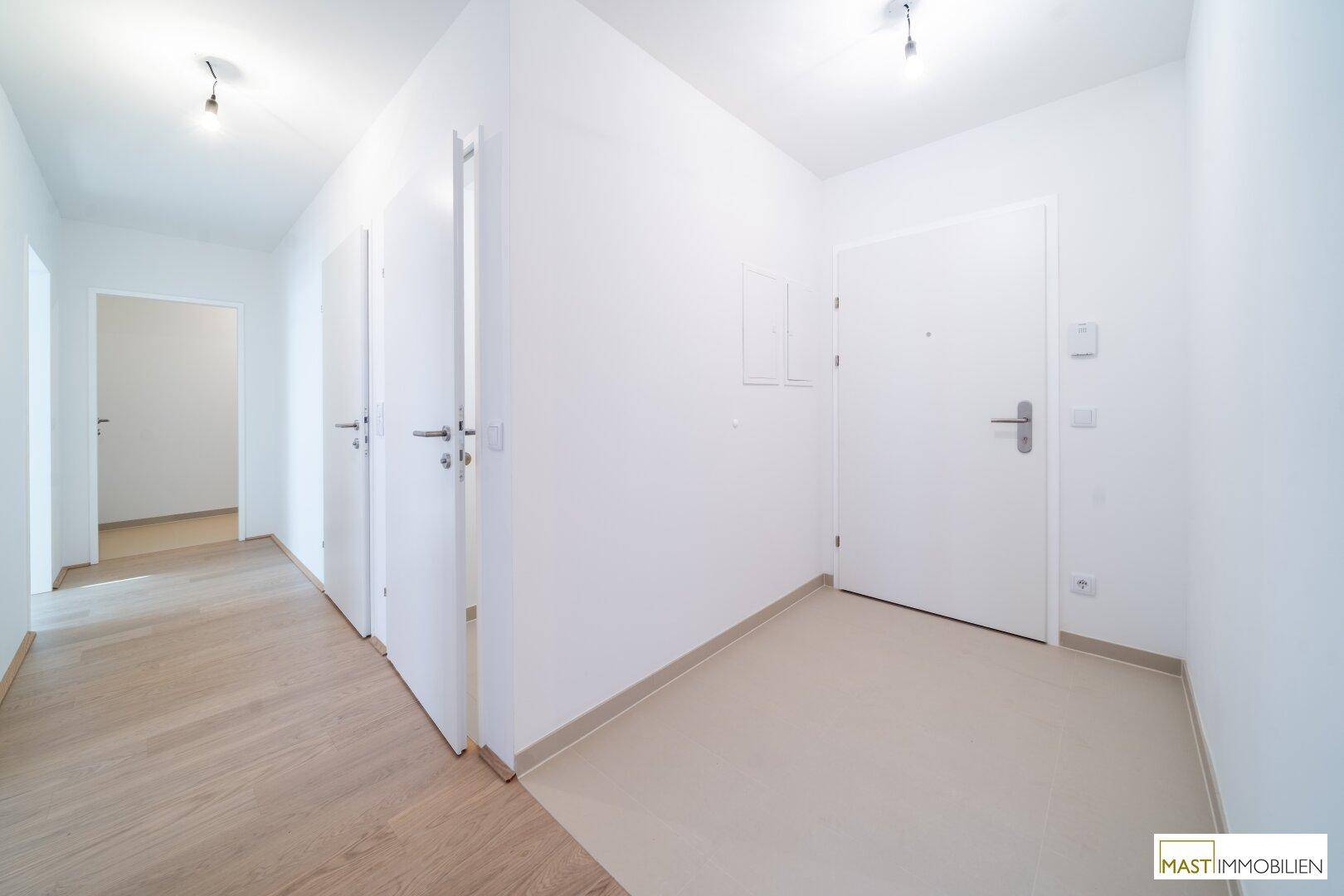 Heller Flur mit zwei verschiedenen Bodenbelägen und mehreren weißen Türen.
