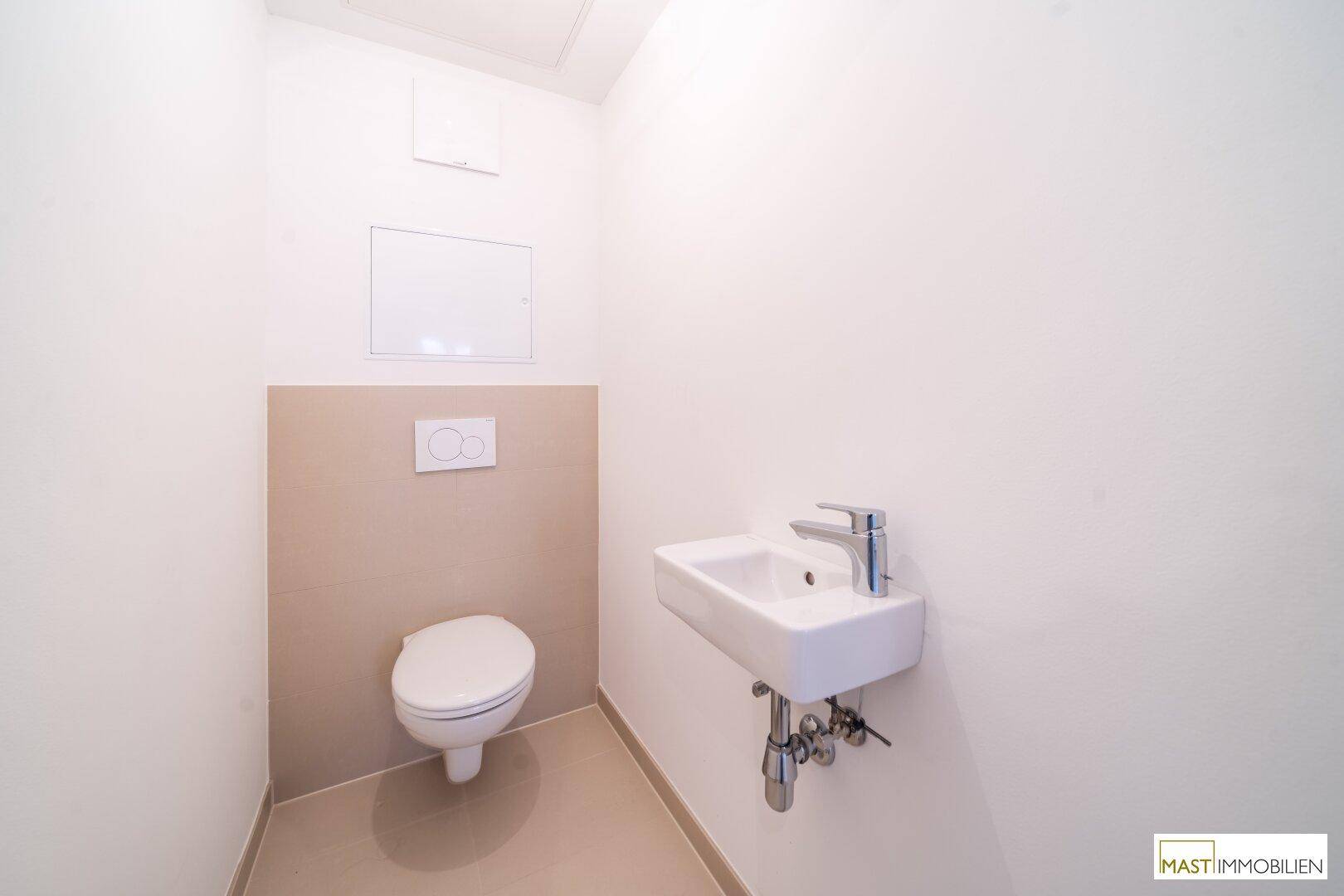 Separate Gästetoilette mit wandmontiertem WC und kleinem Waschbecken.