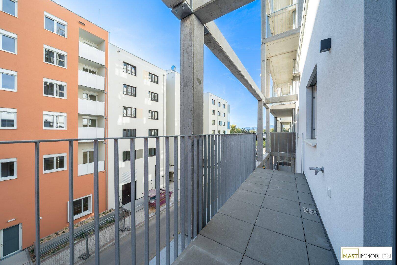 Langer Balkon mit Metallgeländer und Blick auf umliegende Wohngebäude.