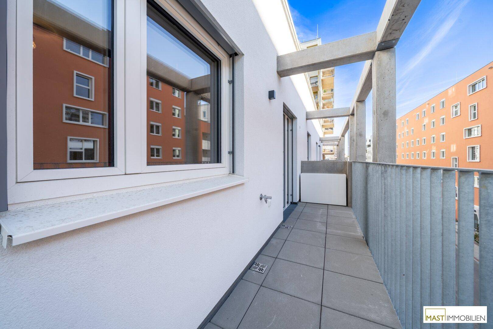 Geräumiger Balkon mit Fliesenboden und Blick auf die moderne Architektur der Nachbargebäude.