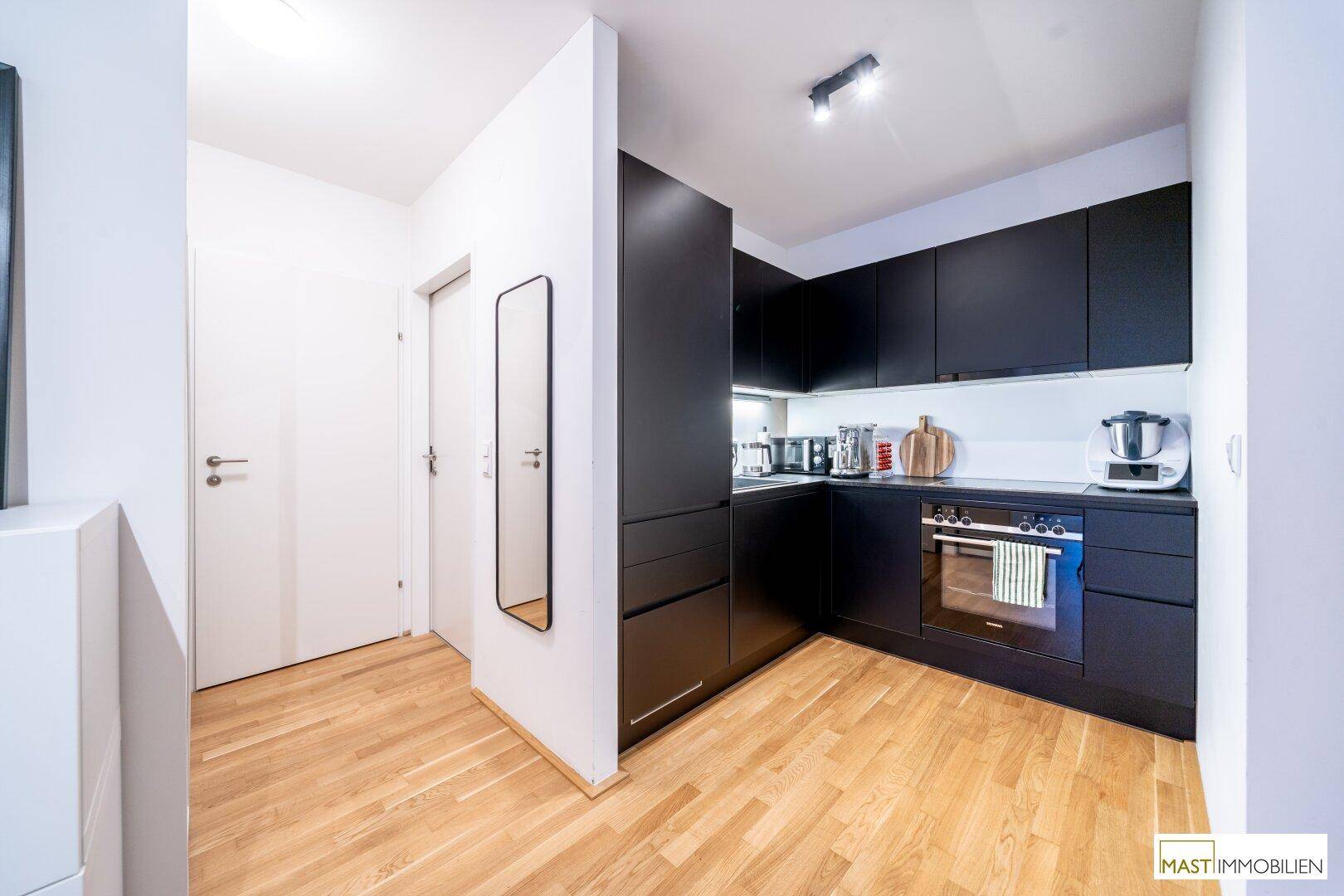 Moderne schwarze Einbauküche mit Holzfußboden und integrierten Geräten.
