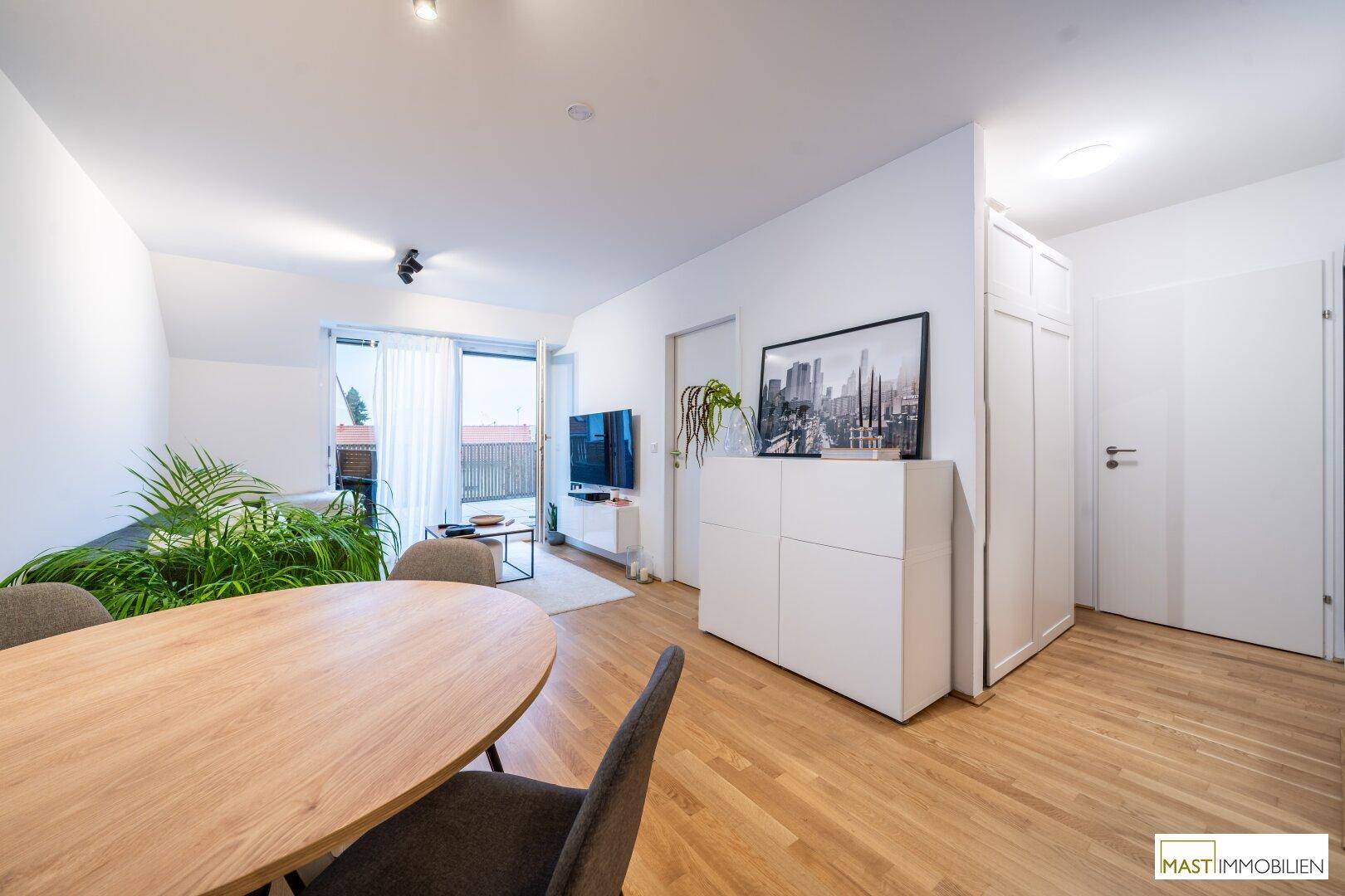 Geräumiger Wohn-Essbereich mit Parkettboden, weißem Mobiliar und Blick zum Balkon.
