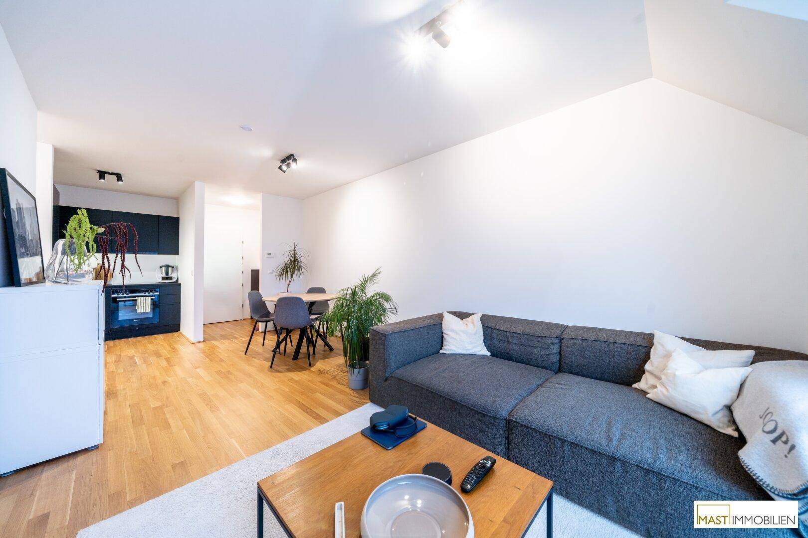 Offener Wohnbereich mit Essplatz, gemütlichem Sofa und angrenzender schwarzer Küche.