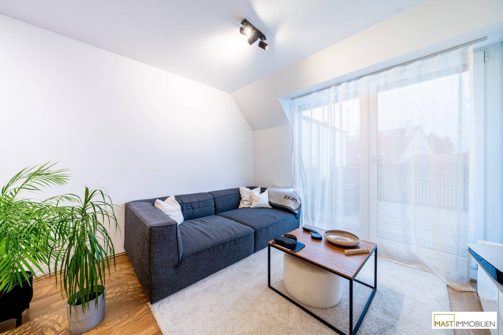 Heller Wohnbereich mit großem Fenster, bequemer Couch und Topfpflanze.
