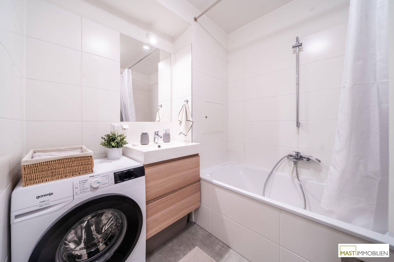 Modernes Badezimmer mit Badewanne, Waschbecken und integrierter Waschmaschine.