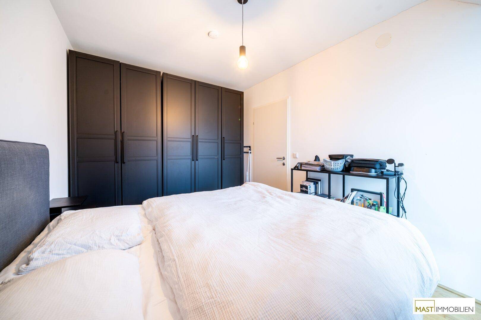 Schlafzimmer mit großem Doppelbett, dunklen Einbauschränken und Holzboden.
