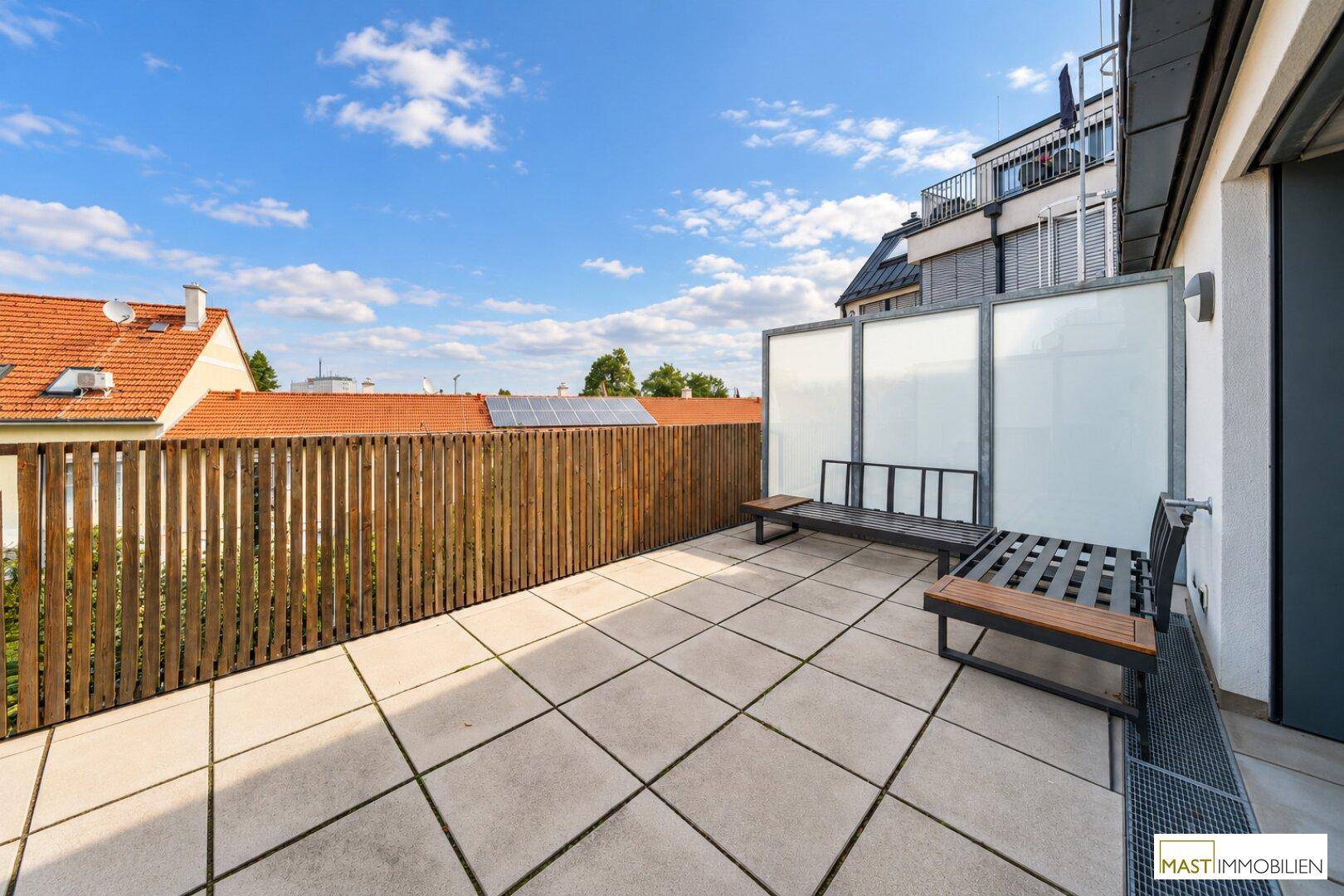 Geräumige Dachterrasse mit Fliesenboden, Holzzaun und Sitzgelegenheiten.