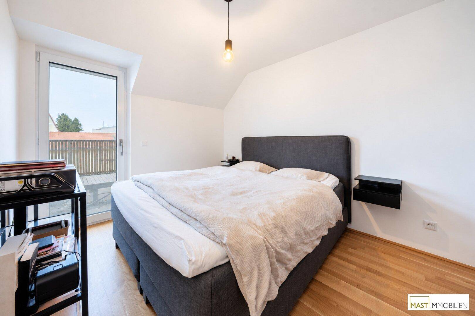 Helles Schlafzimmer mit Doppelbett, Holzboden und direktem Zugang zum Balkon.