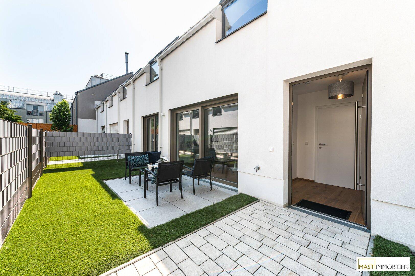Sonniger Außenbereich mit gepflasterter Terrasse, Rasenfläche und direktem Zugang zum Haus.