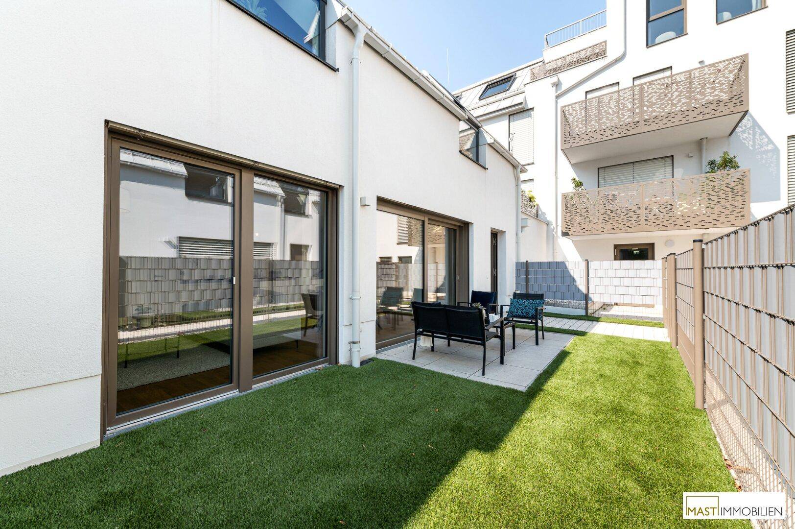 Geräumige Terrasse mit Sitzgelegenheiten und angrenzendem Gartenbereich, umgeben von einem Zaun.